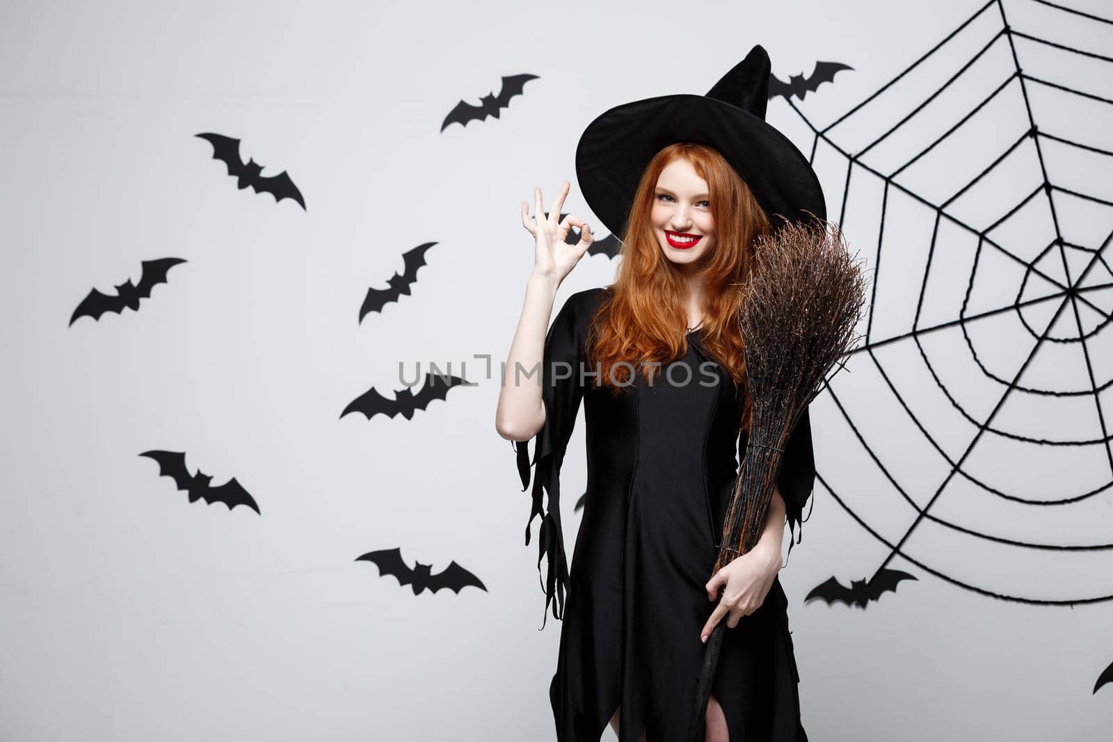 Halloween Concept - Happy elegant witch enjoy playing with broomstick halloween party over grey background. by Benzoix