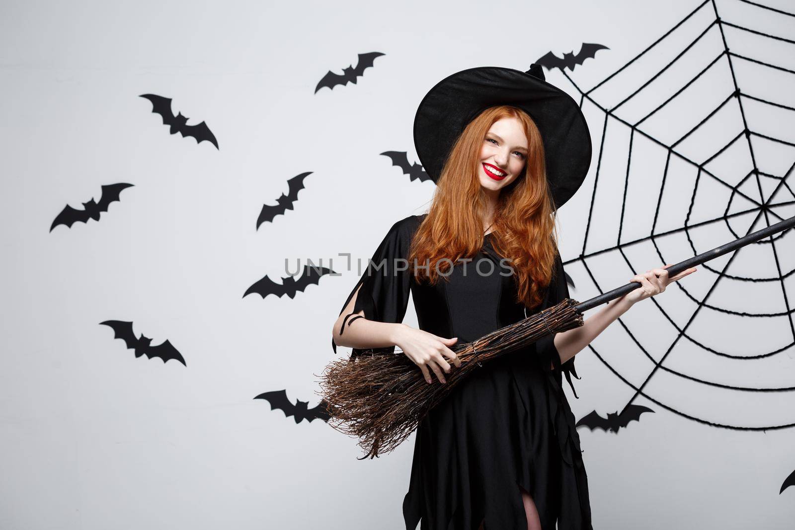 Halloween Concept - Happy elegant witch enjoy playing with broomstick halloween party over grey background. by Benzoix