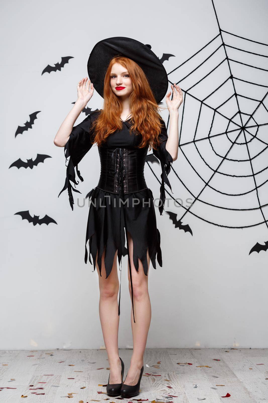Halloween witch concept - Full-length of Happy Halloween Witch holding posing over dark grey studio background with bat and spider web