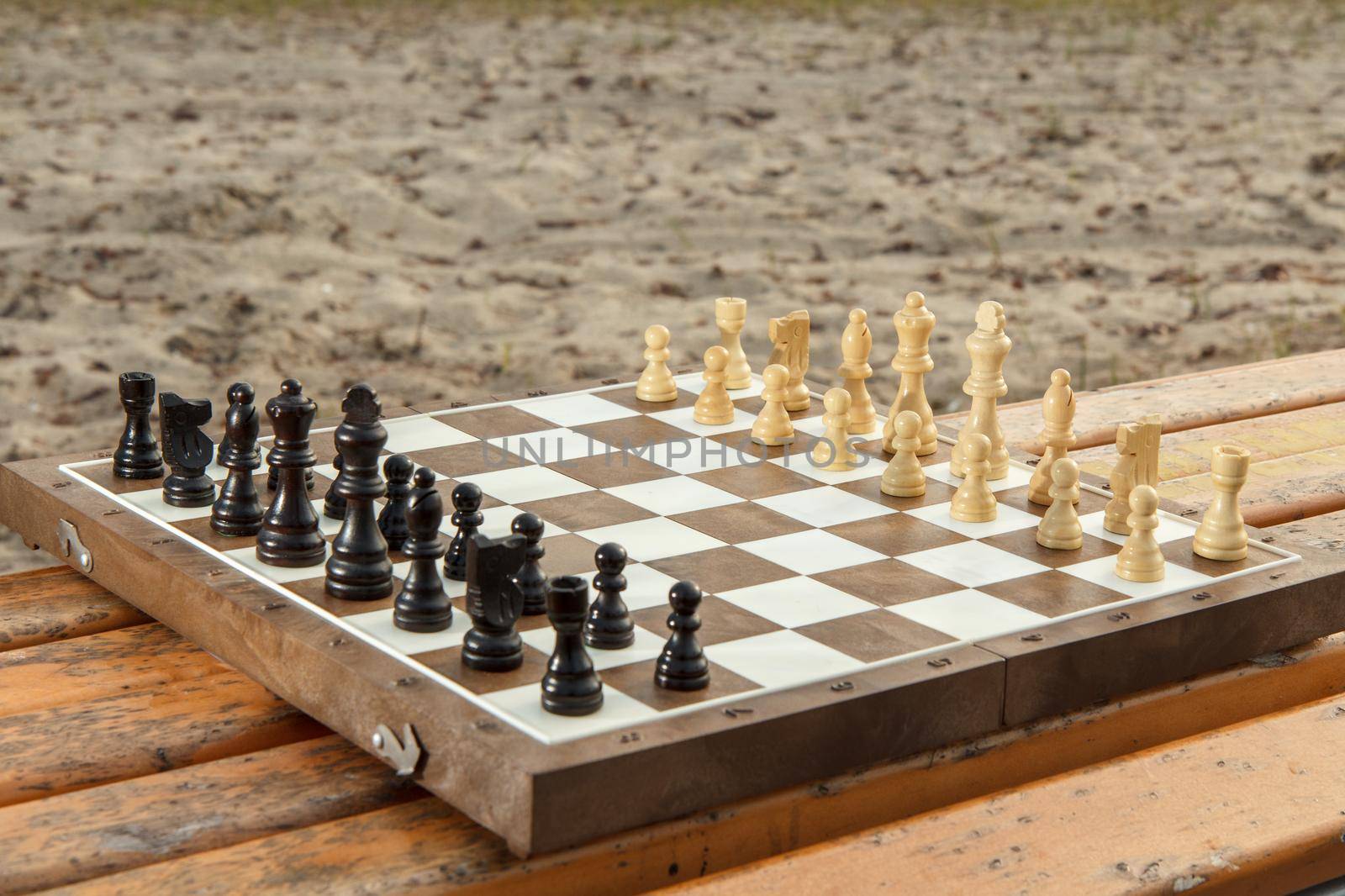 Chess board with chess pieces on wooden bench. Outdoors chess game with wooden chess pieces