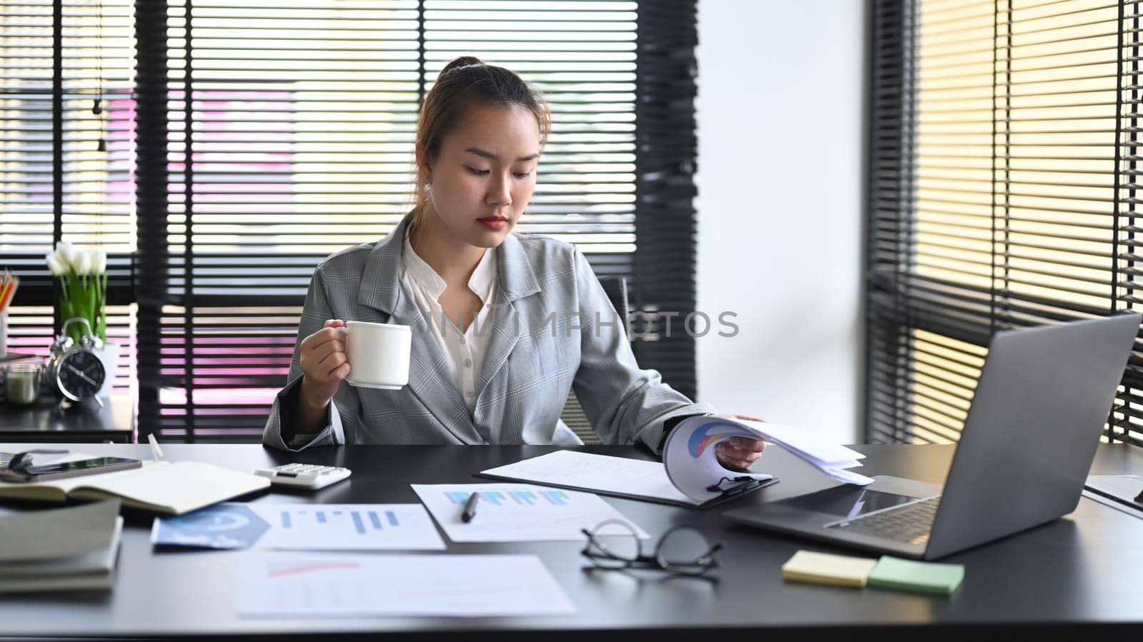 Professional businesswoman drinking coffee and working at modern office.