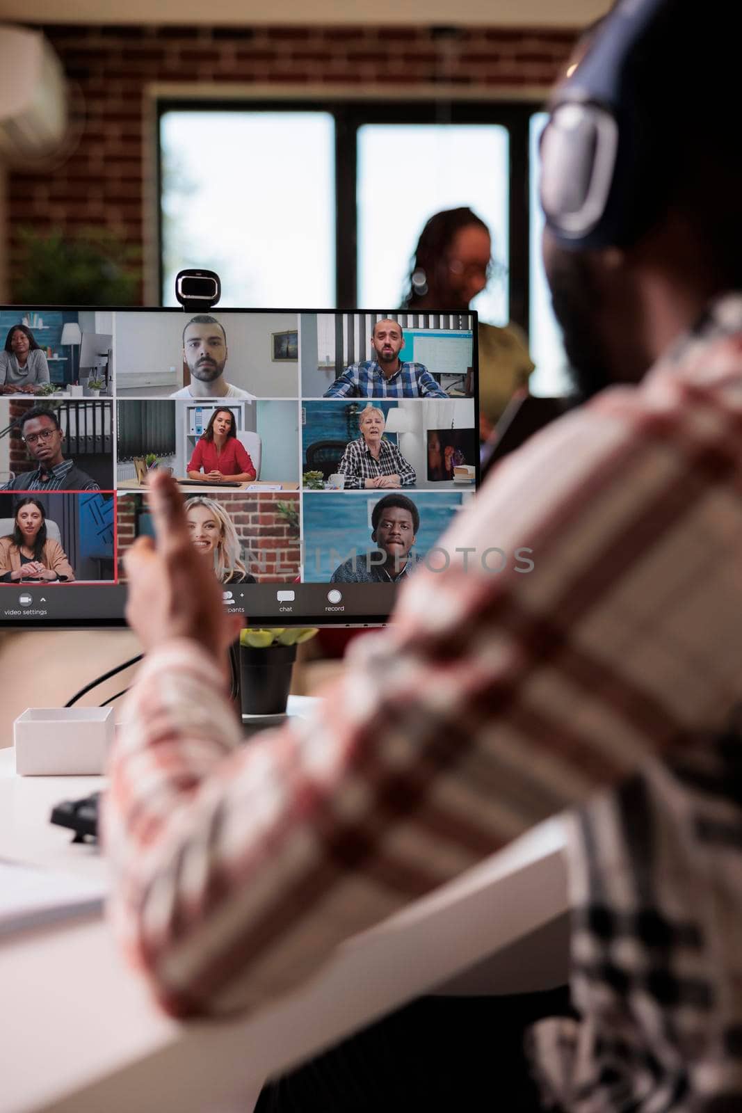 African american with wireless headphones working from home gesturing in video call with colleagues at desk in living room. Startup employee talking with team in internet conference on personal computer.