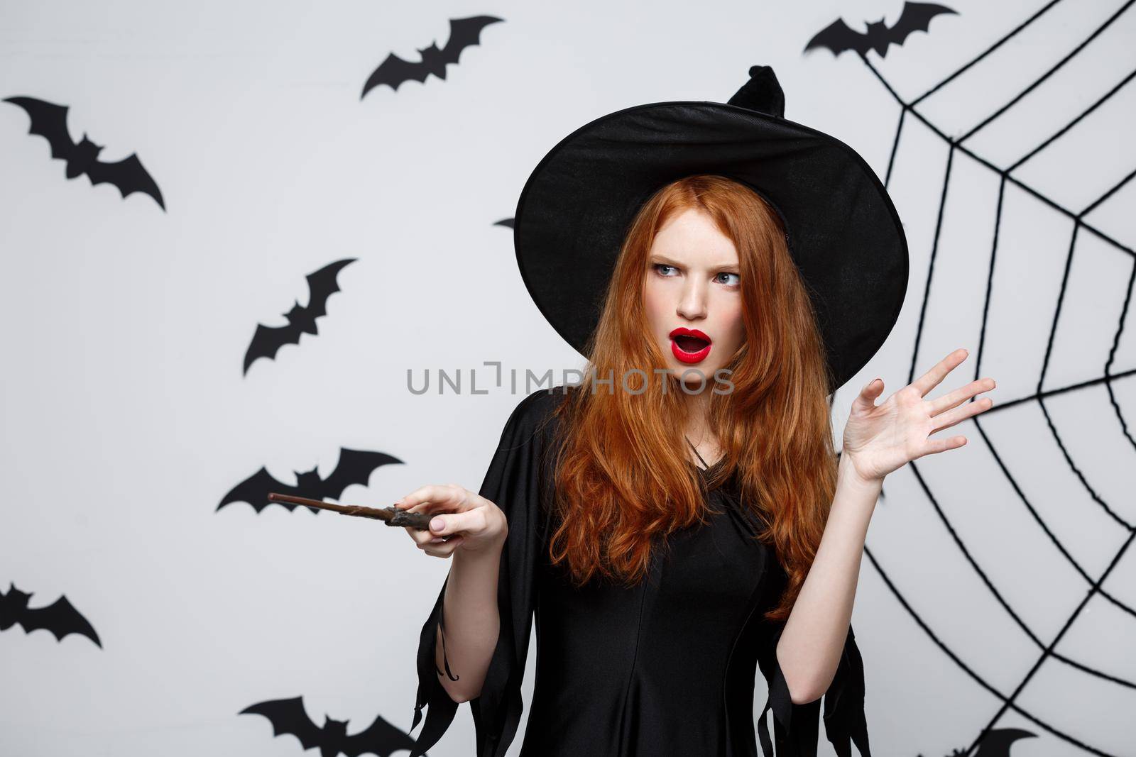 Halloween Concept - Beautiful Witch playing with magic stick on grey background. by Benzoix