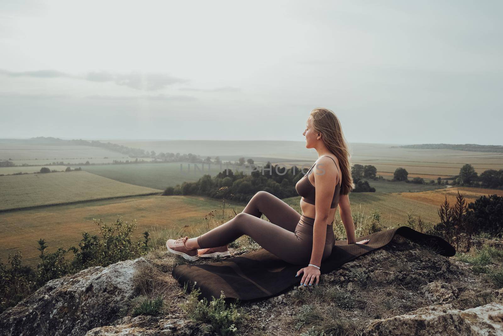 Young Woman Sitting on Top of Hill Outdoors, Sporty Girl Enjoying Panoramic Landscape at Sunset