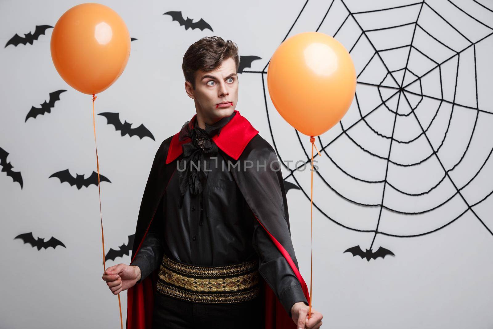 Portrait of handsome caucasian in Vampire halloween costume with colorful Balloon. by Benzoix