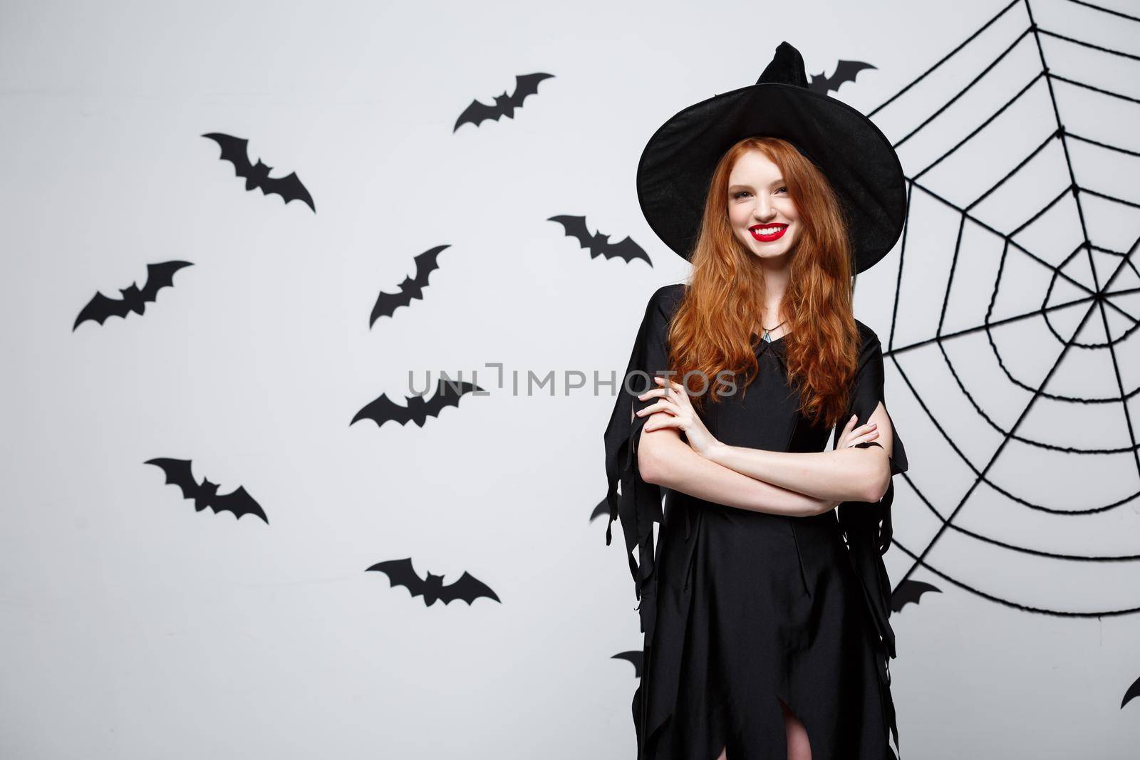 Halloween witch concept - Happy Halloween Witch holding posing over dark grey studio background with bat and spider web. by Benzoix