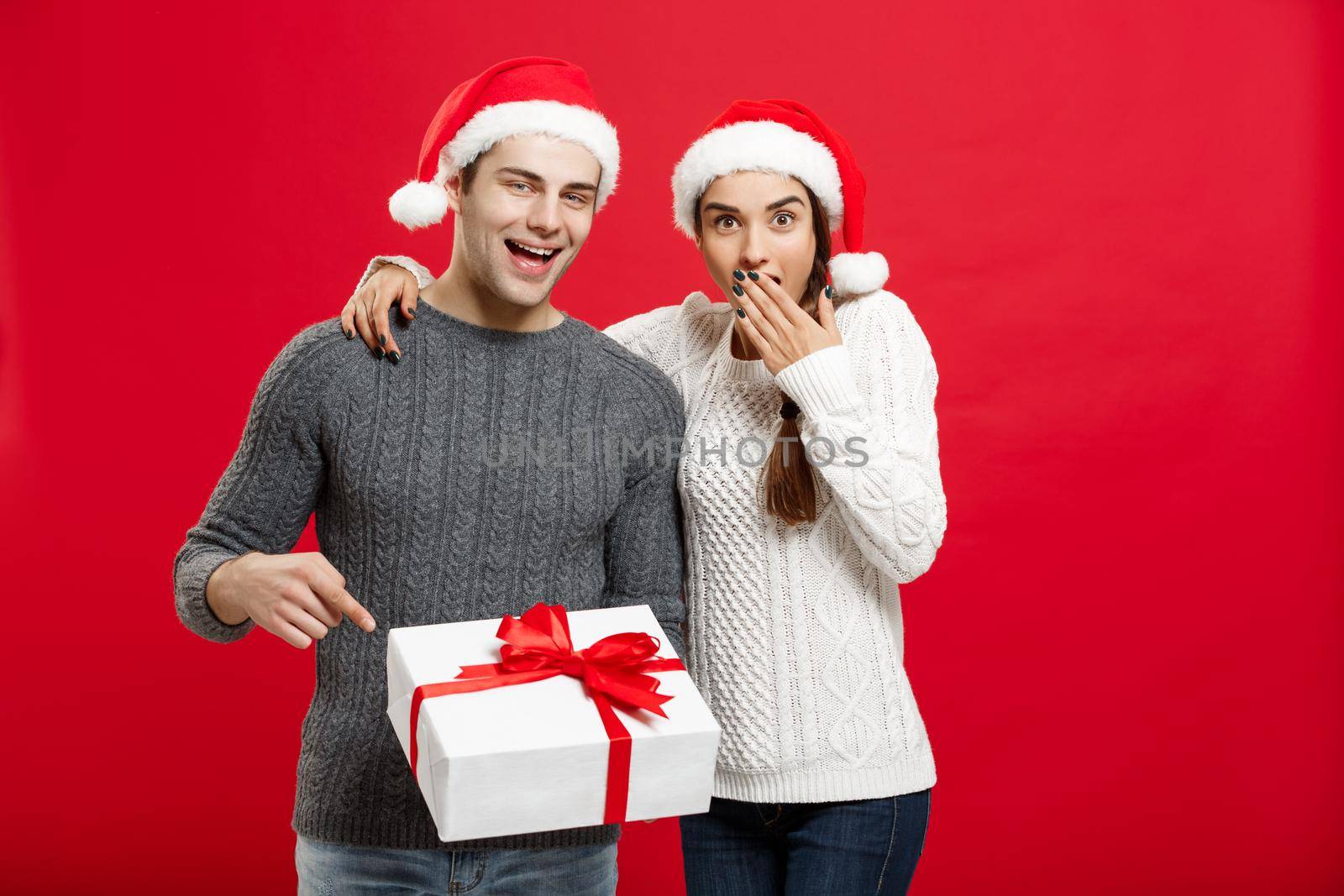 Christmas Concept - portrait young couple in Christmas sweater pointing finger gesture to gifts.