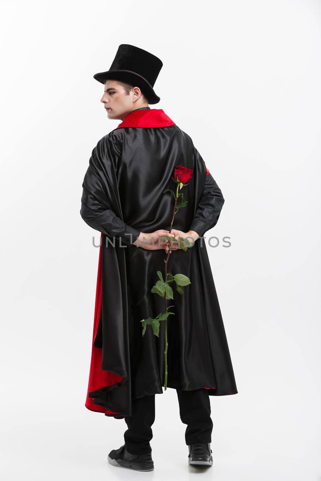 Vampire Halloween Concept - Portrait of handsome caucasian Vampire holding red beautiful rose. by Benzoix