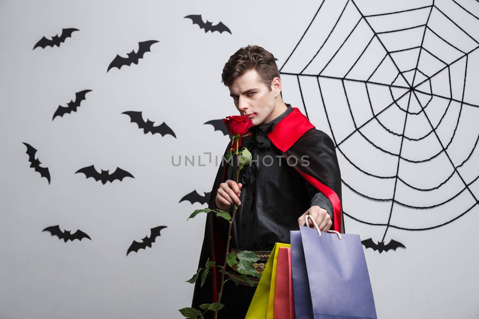 Vampire Halloween Concept - Happy handsome caucasian Vampire holding colorful shopping bag