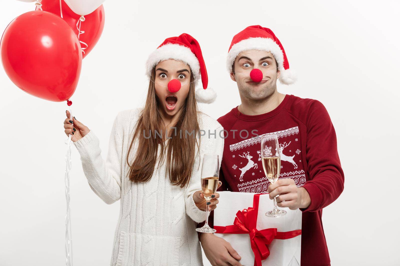 Christmas Concept - Young caucasian couple holding gifts,champagne and balloon making funny face on Christmas.