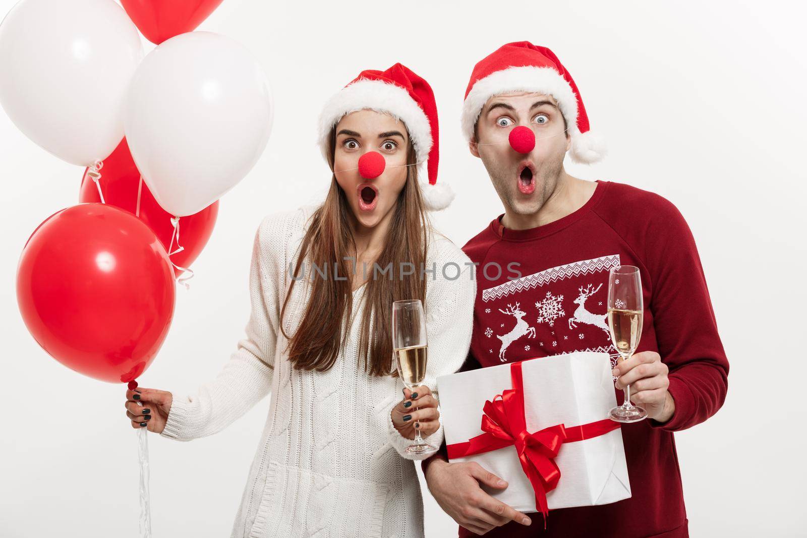 Christmas Concept - Young caucasian couple holding gifts,champagne and balloon making funny face on Christmas by Benzoix