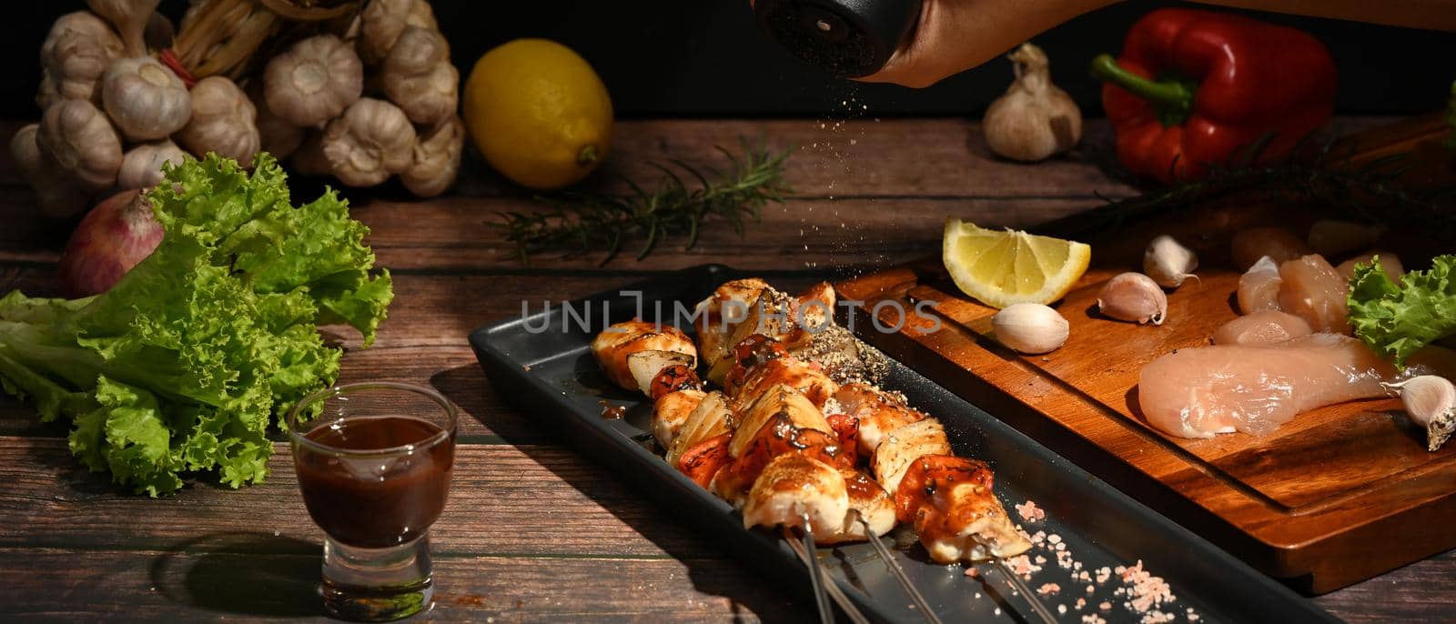 Grilled skewers of chicken, bell peppers, tomatoes, onion and barbecue sauce on wooden background.
