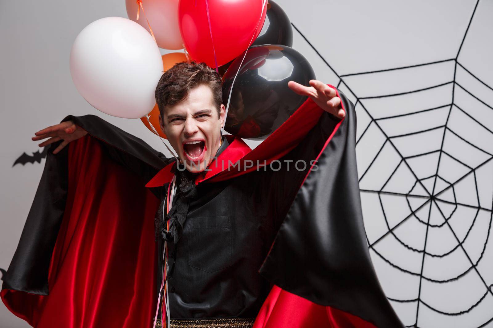 Vampire Halloween Concept - Portrait of handsome caucasian in Vampire halloween costume with colorful Balloon.