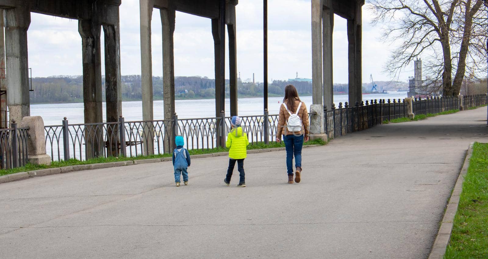 A mother and two small children walk along the embankment on a clear spring day.