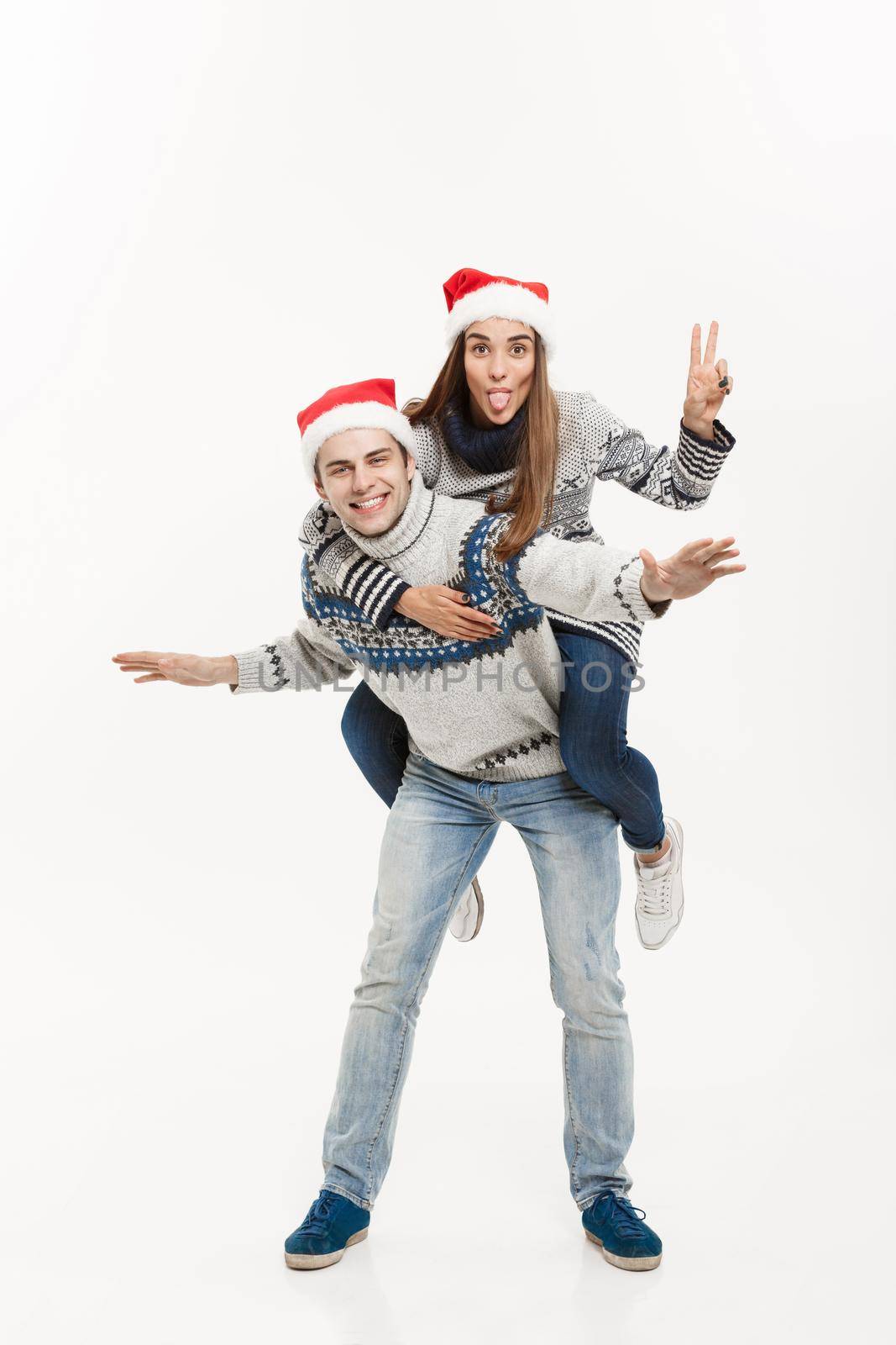 Christmas Concept - Young happy couple in sweaters enjoying piggyback ride isolated on white grey background.