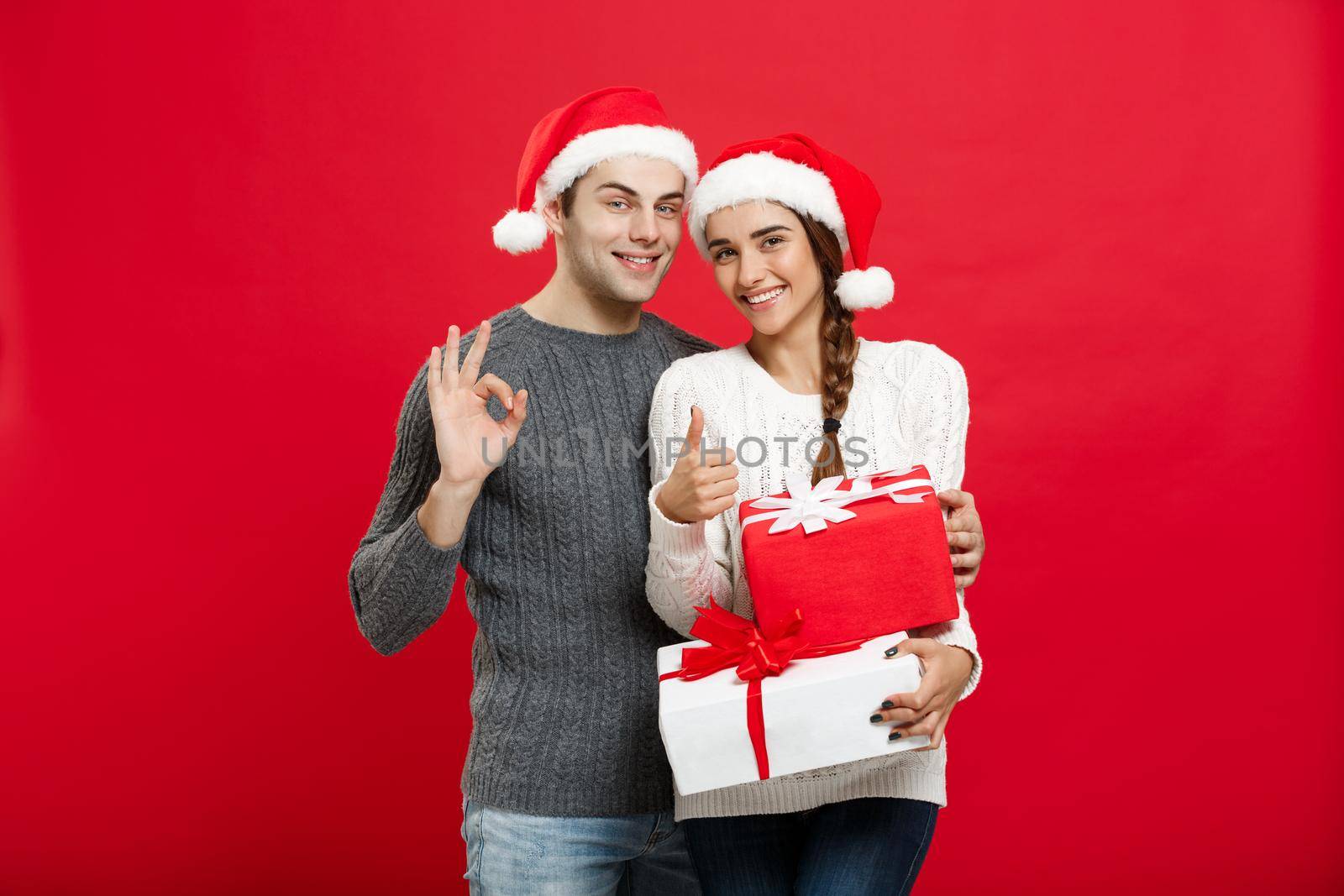 Christmas Concept - portrait young couple in Christmas sweater showing ok gesture with gifts.