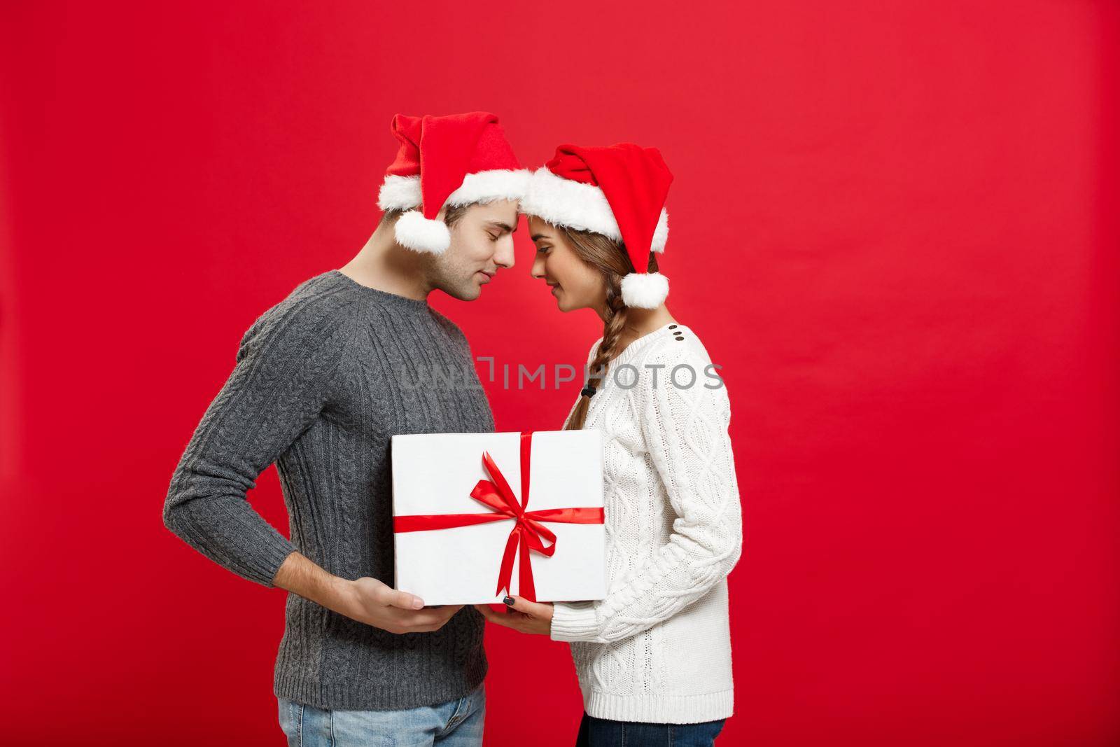 Christmas Concept - isolated lovely young couple holding tight with white gift over red background.