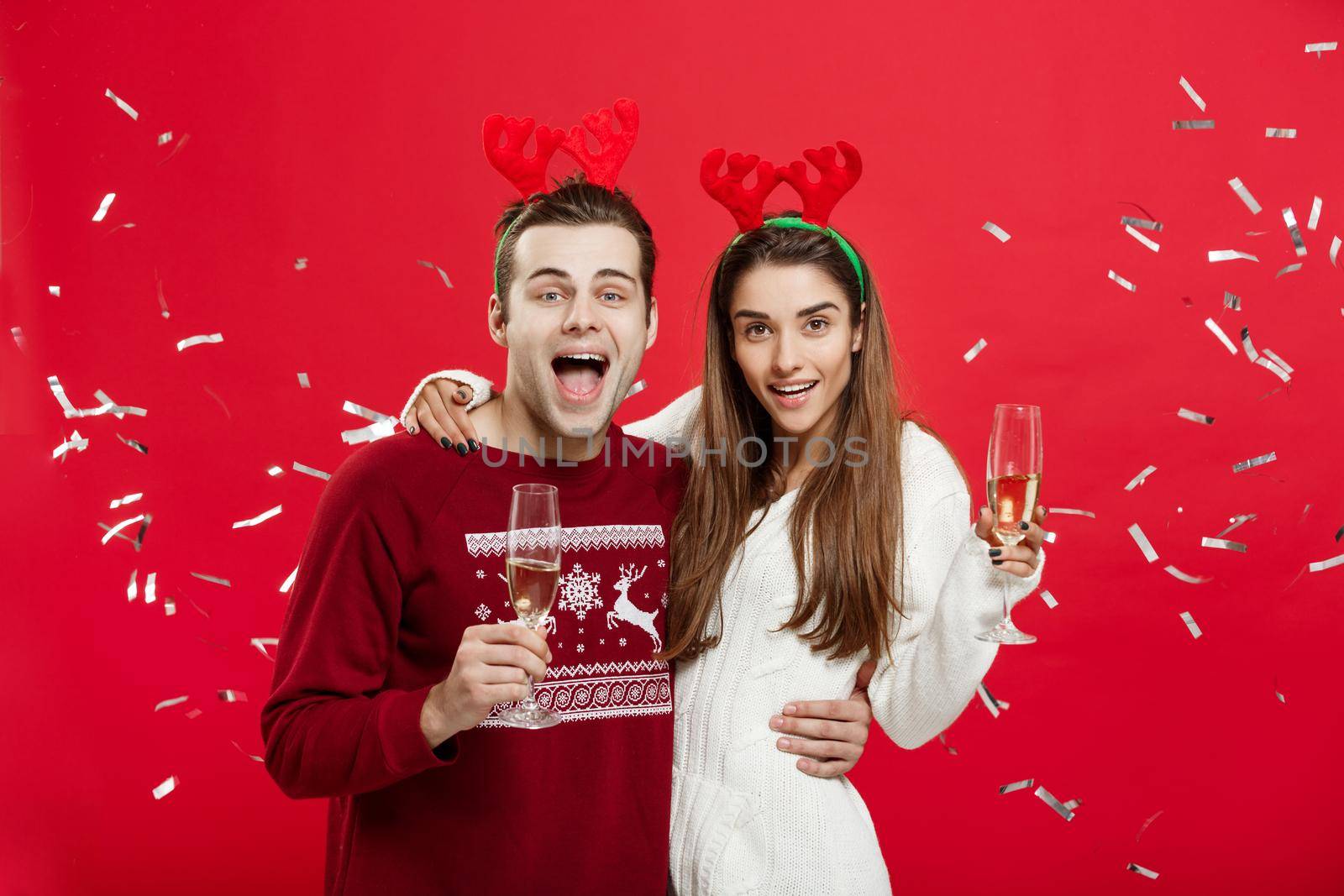 Christmas Concept - Happy caucasian man and woman in reindeer hats celebrating christmas toasting with champagne flutes, congratulating on xmas.