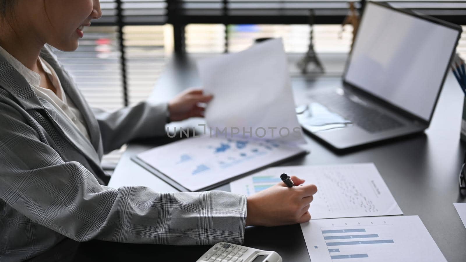 Concentrated female director reviewing financial charts and graphs data in document at office desk.