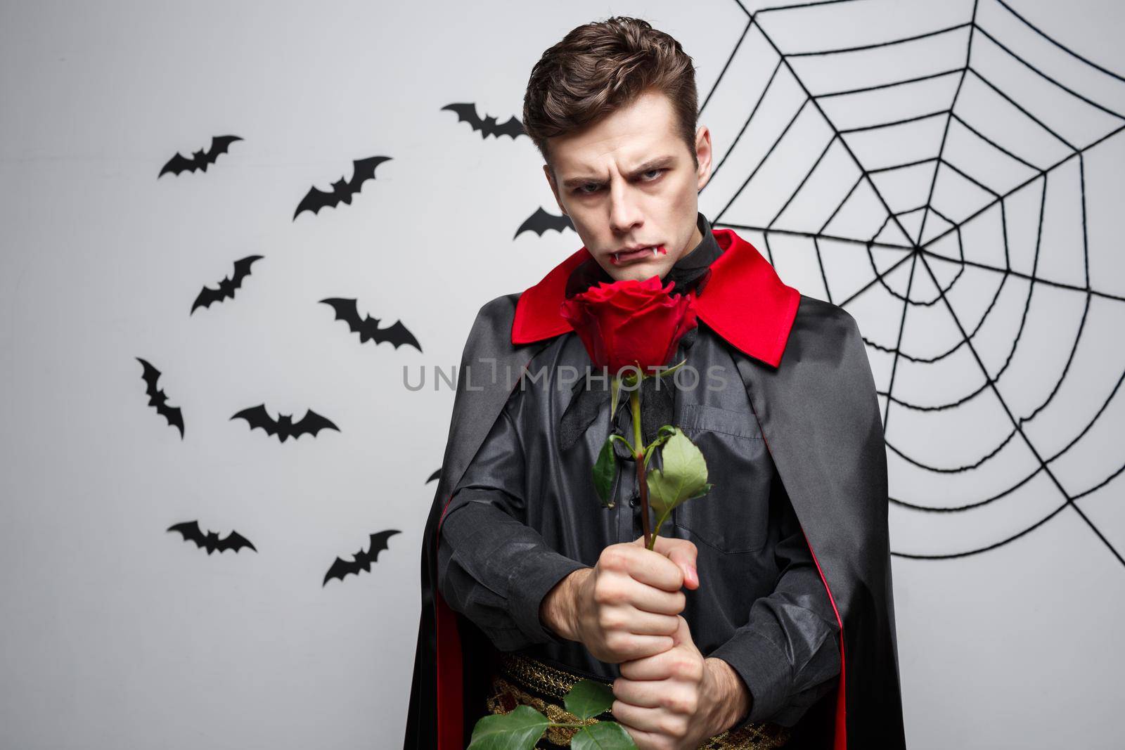Vampire Halloween Concept - Portrait of handsome caucasian Vampire holding red beautiful rose. by Benzoix