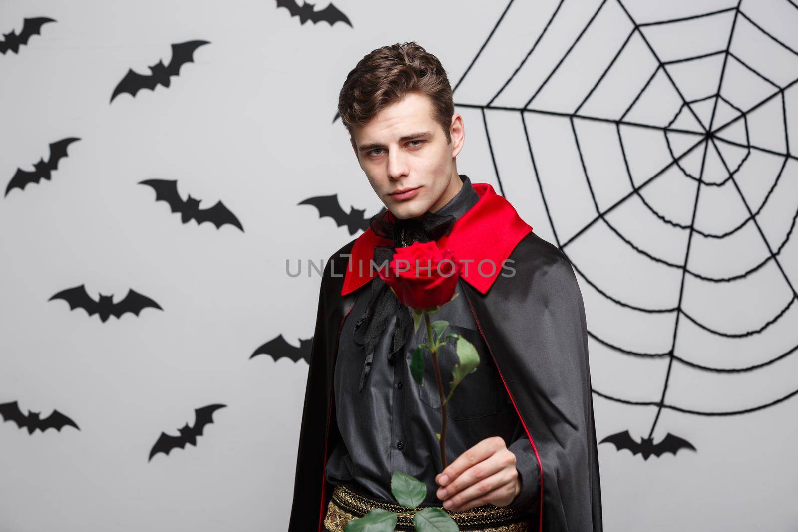 Vampire Halloween Concept - Portrait of handsome caucasian Vampire holding red beautiful rose