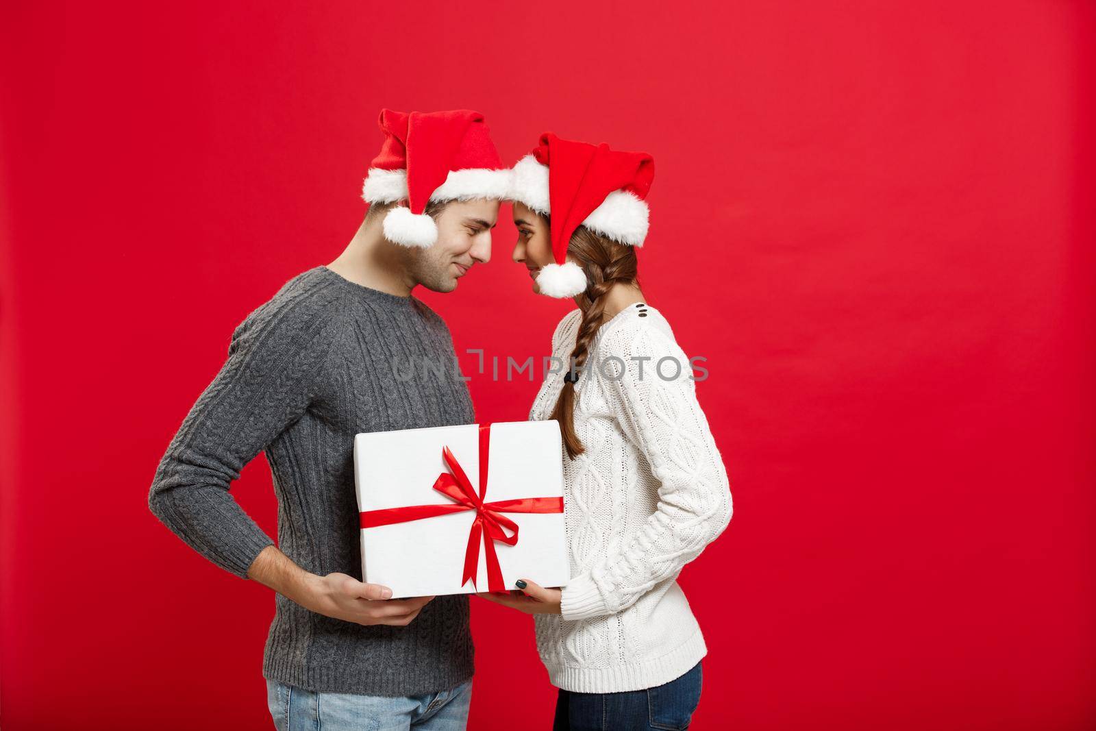 Christmas Concept - isolated lovely young couple holding tight with white gift over red background by Benzoix