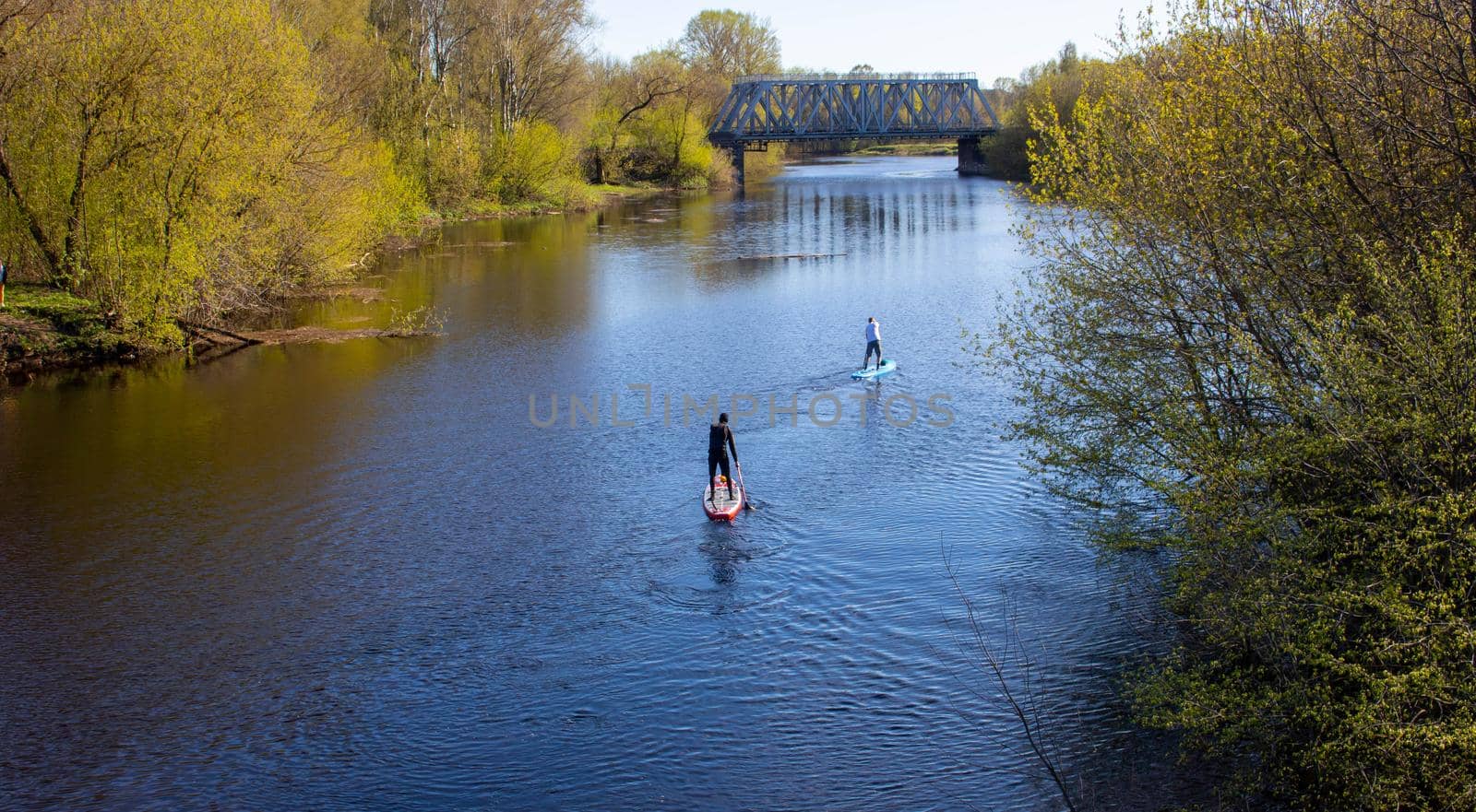 Two men are swimming on a paddleboard on the spring river.I can't see his face