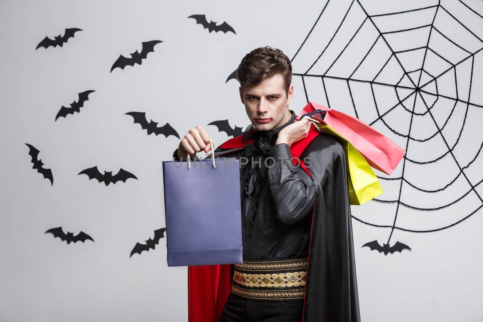 Vampire Halloween Concept - Happy handsome caucasian Vampire holding colorful shopping bag