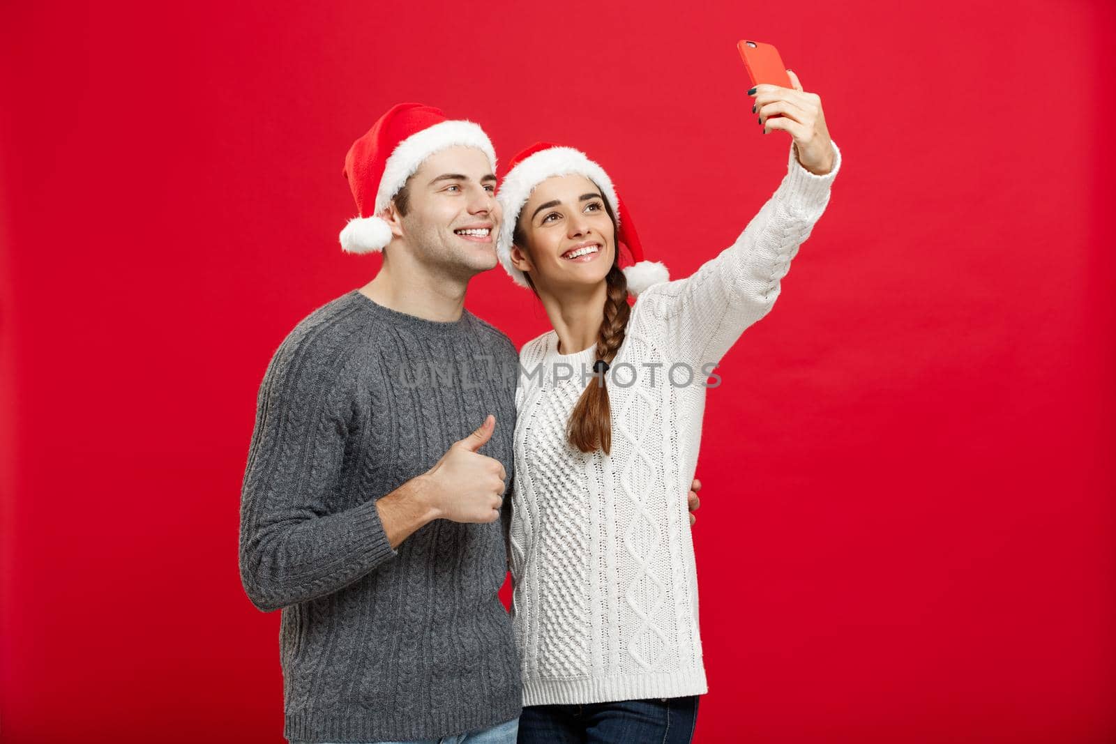 Christmas Concept - Young attractive couple taking a selfie by mobile phone celebrating in Christmas day.
