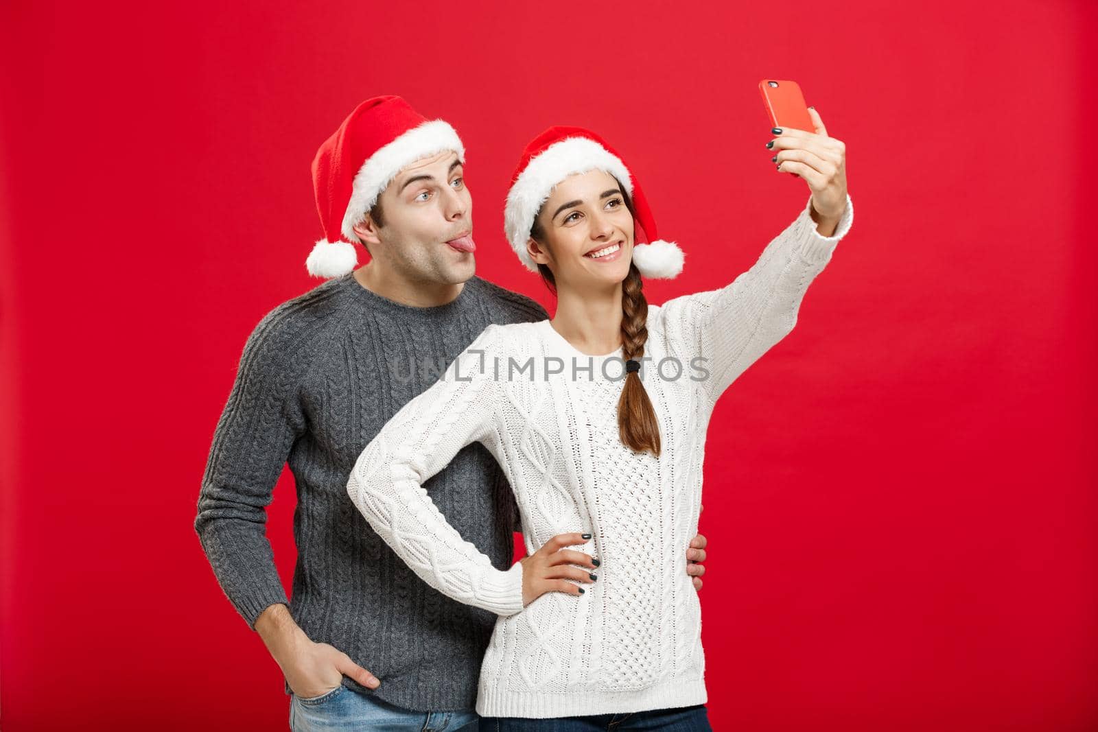 Christmas Concept - Young attractive couple taking a selfie by mobile phone celebrating in Christmas day.