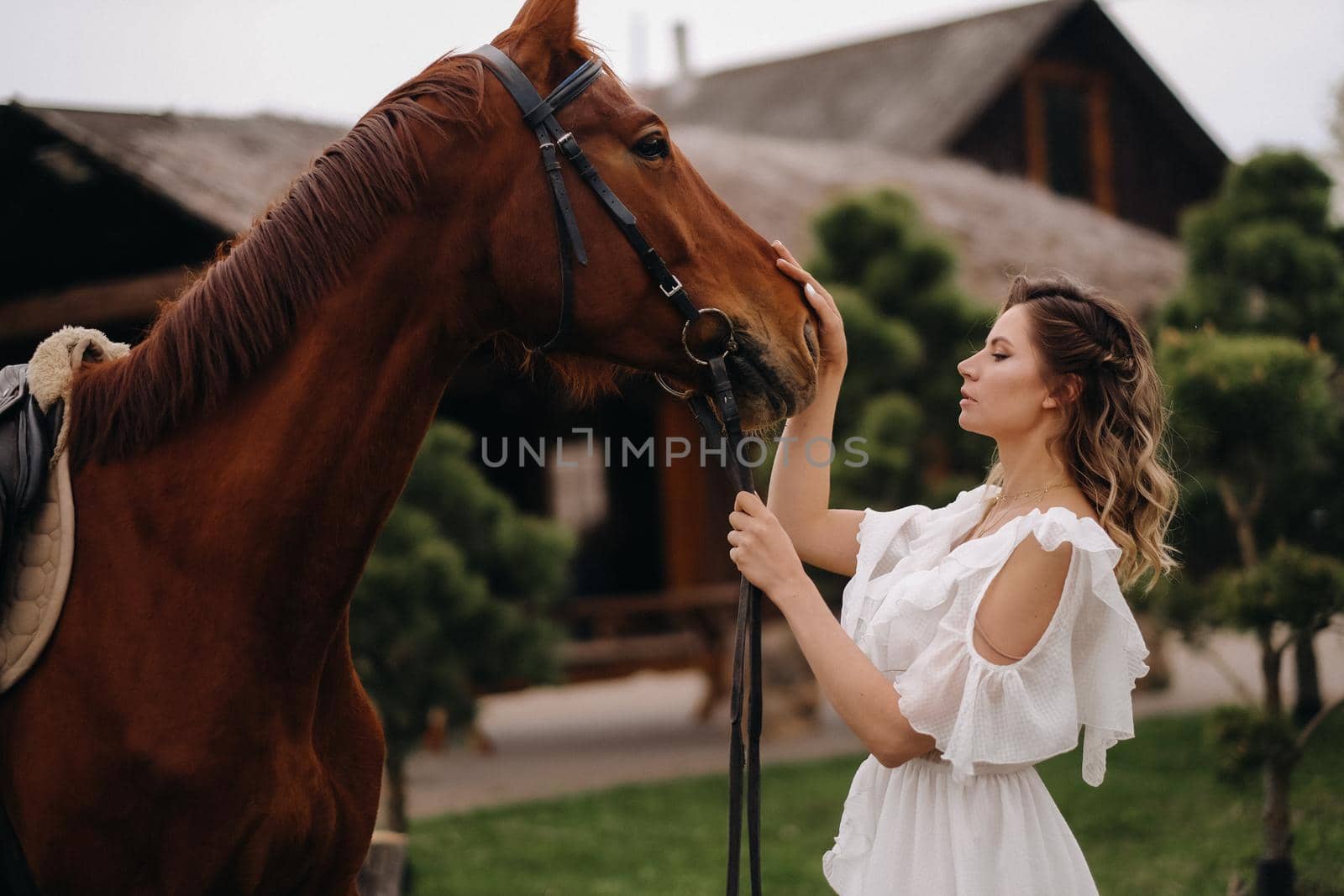 Beautiful girl in a white sundress next to a horse on an old ranch.