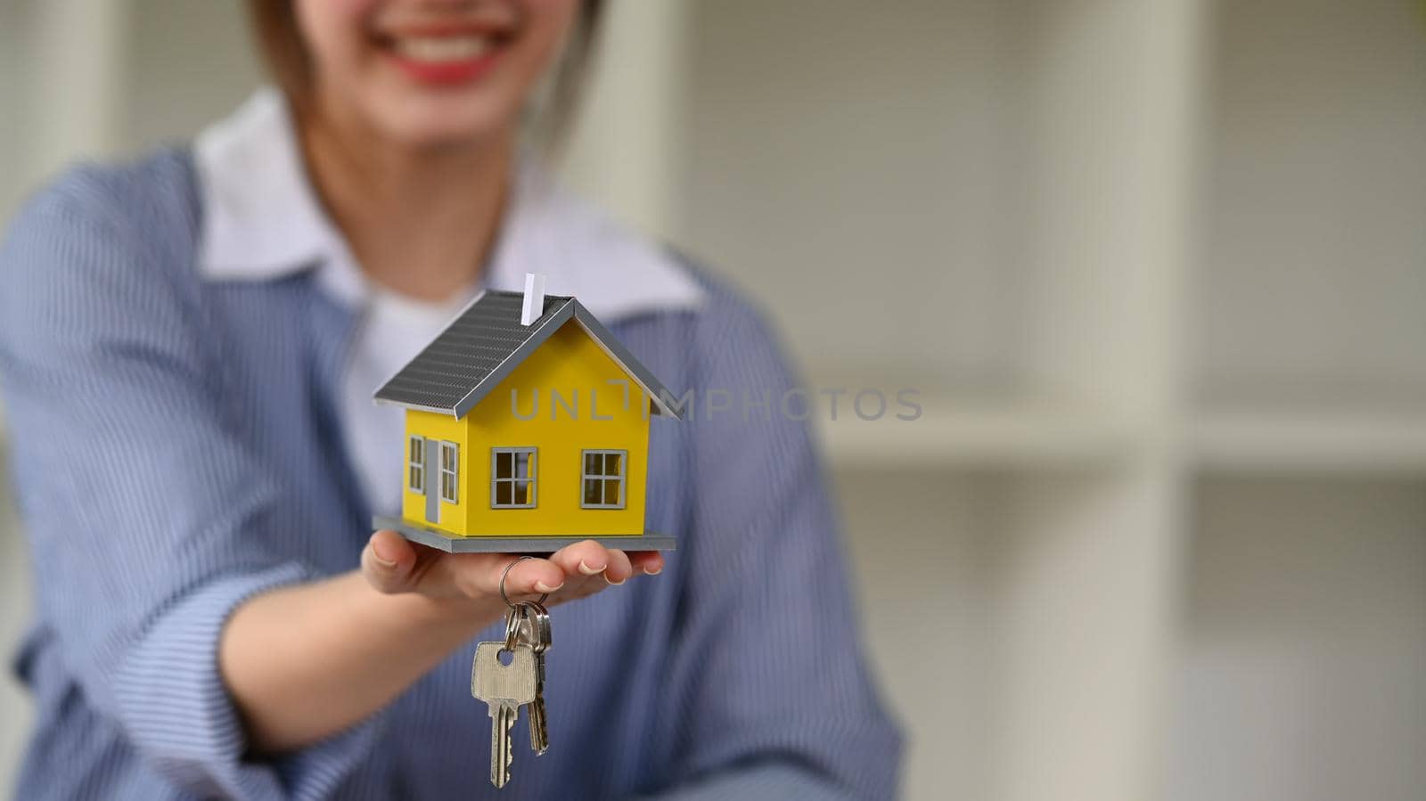 Smiling female financial advisor hand holding house model and keys. New house, insurance and real estate concept.