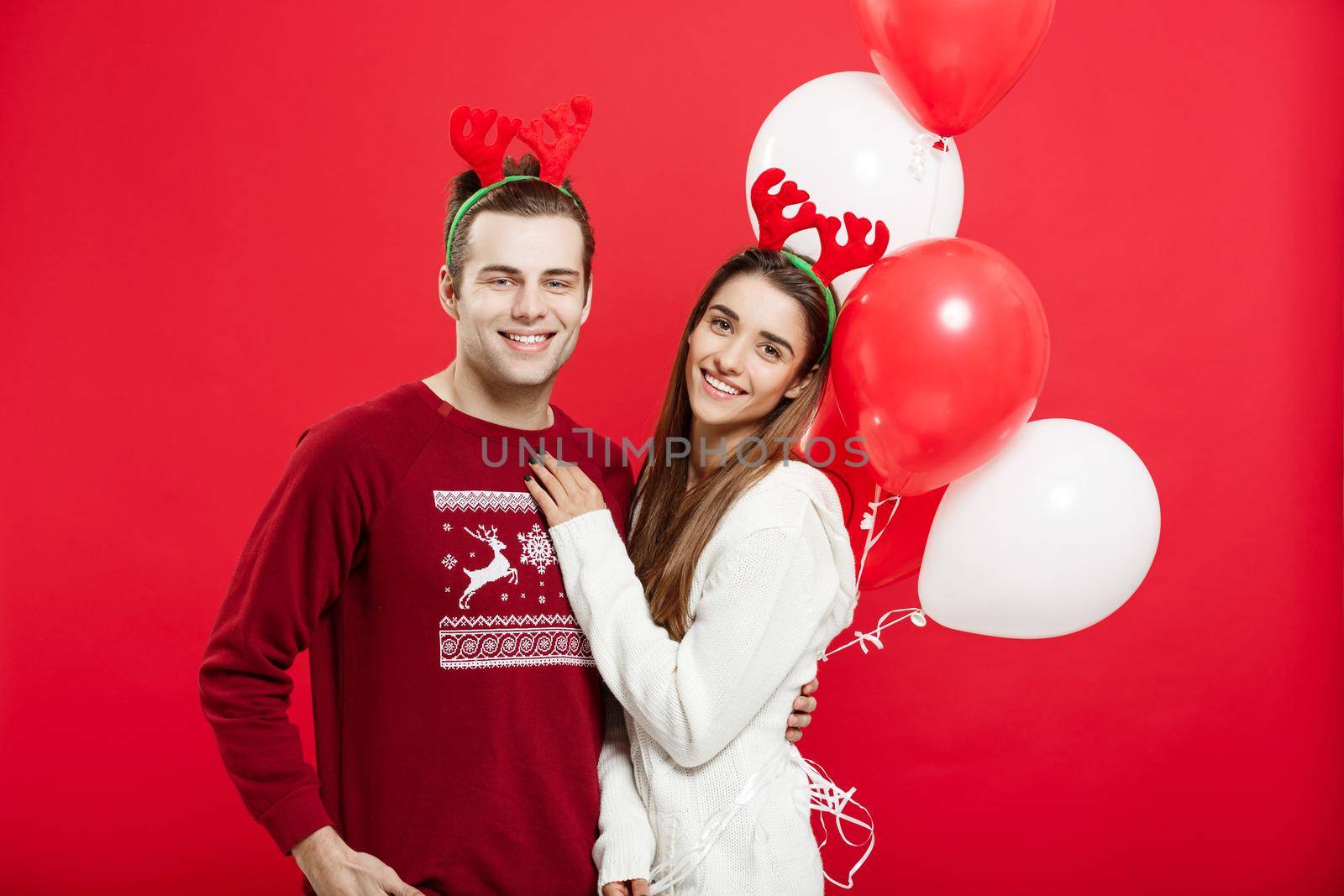 Christmas concept - Portrait of a romantic young couple with christmas balloon over red studio background.