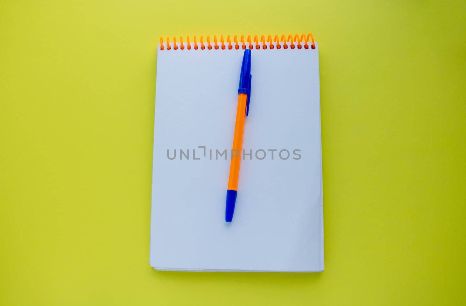 Notepad with an orange spiral and an orange pen, on a yellow background. top view copy space by lapushka62