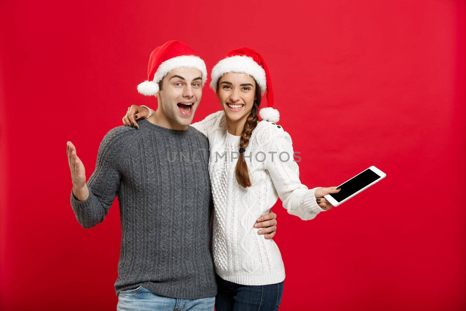 Christmas concept - Happy young couple in christmas sweaters holding digital tablet.