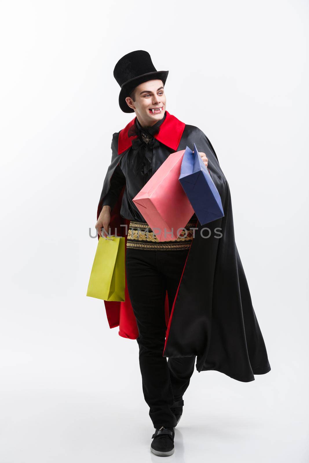 Vampire Halloween Concept - Happy handsome caucasian Vampire holding colorful shopping bag on white background