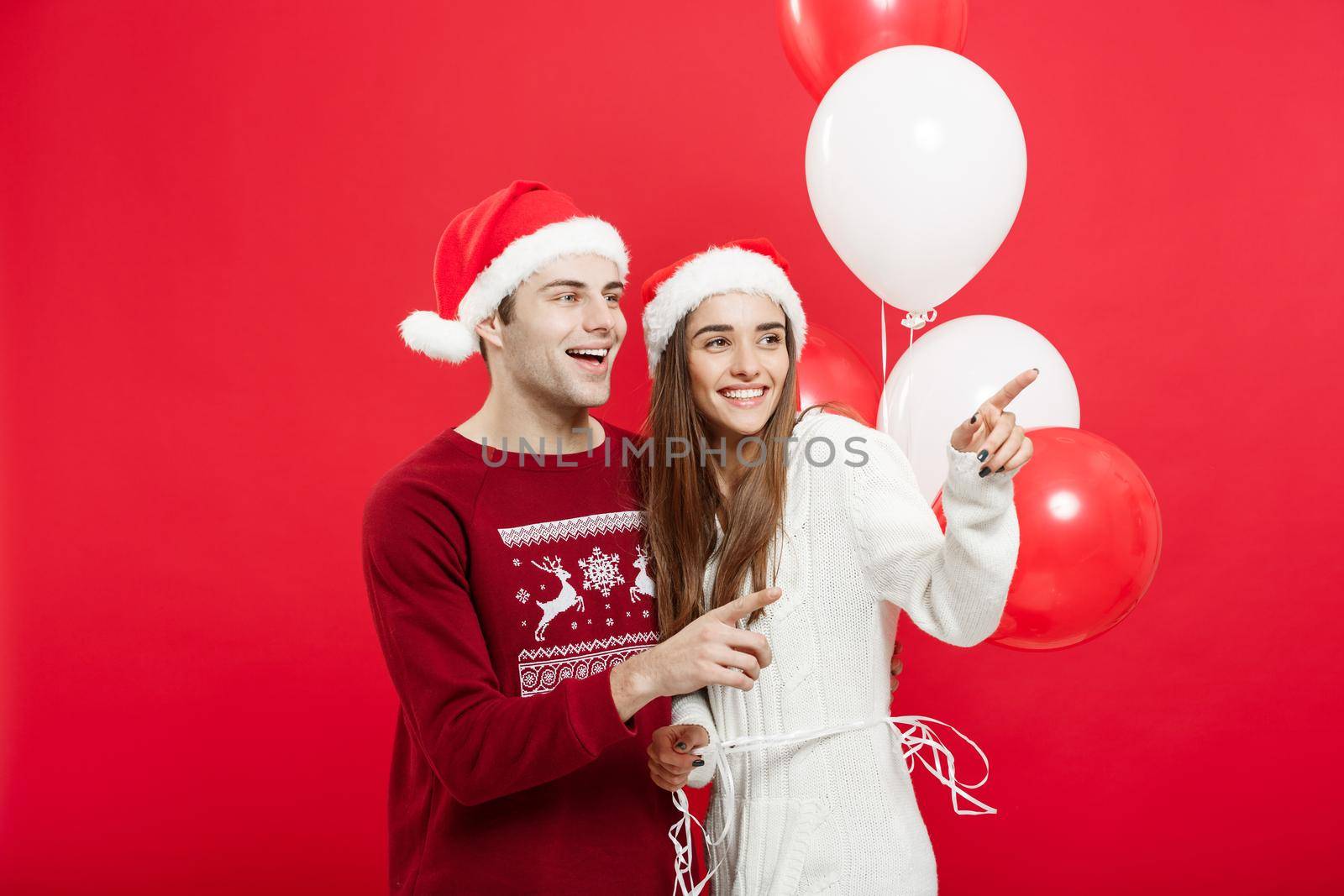 Christmas concept - Portrait of a romantic young couple with christmas balloon over red studio background.