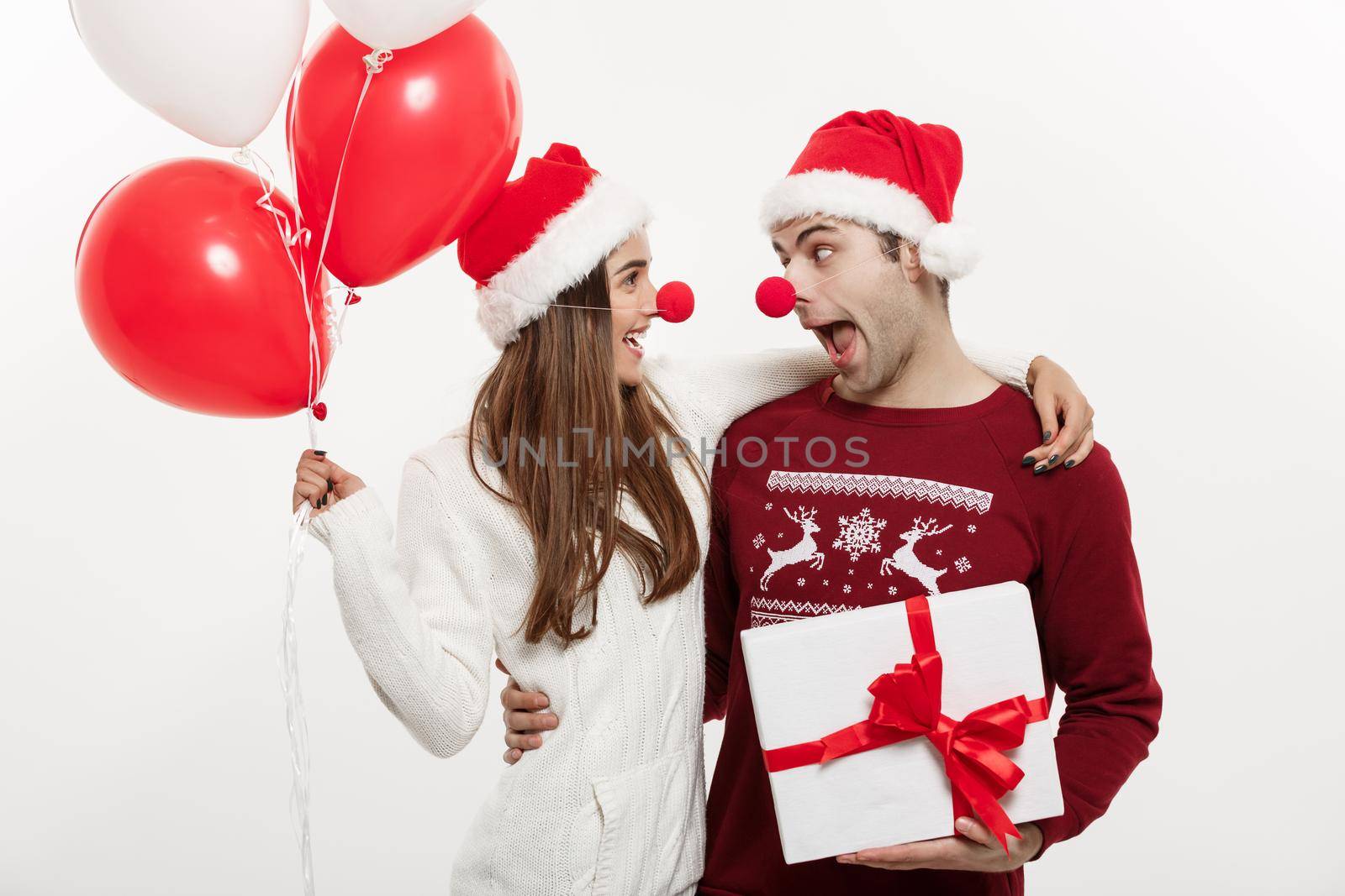 Christmas Concept - Young caucasian couple holding gifts,champagne and balloon making funny face on Christmas by Benzoix