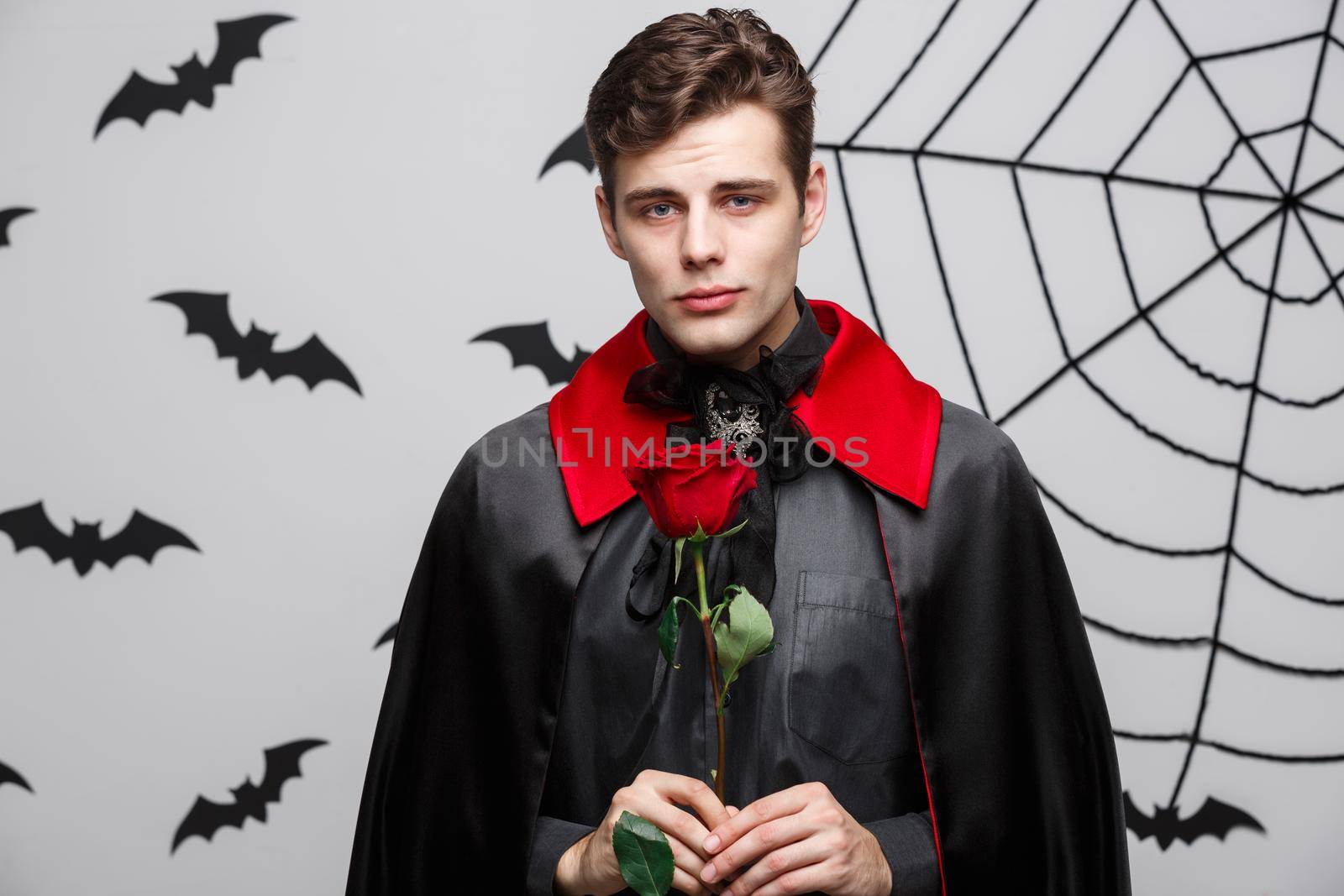 Vampire Halloween Concept - Portrait of handsome caucasian Vampire holding red beautiful rose. by Benzoix