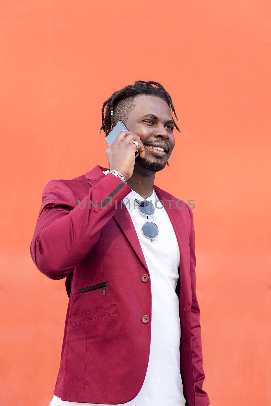 vertical photo of a stylish african businessman in suit smiling and talking on phone in front of red background, copy space for text, concept of technology and communication