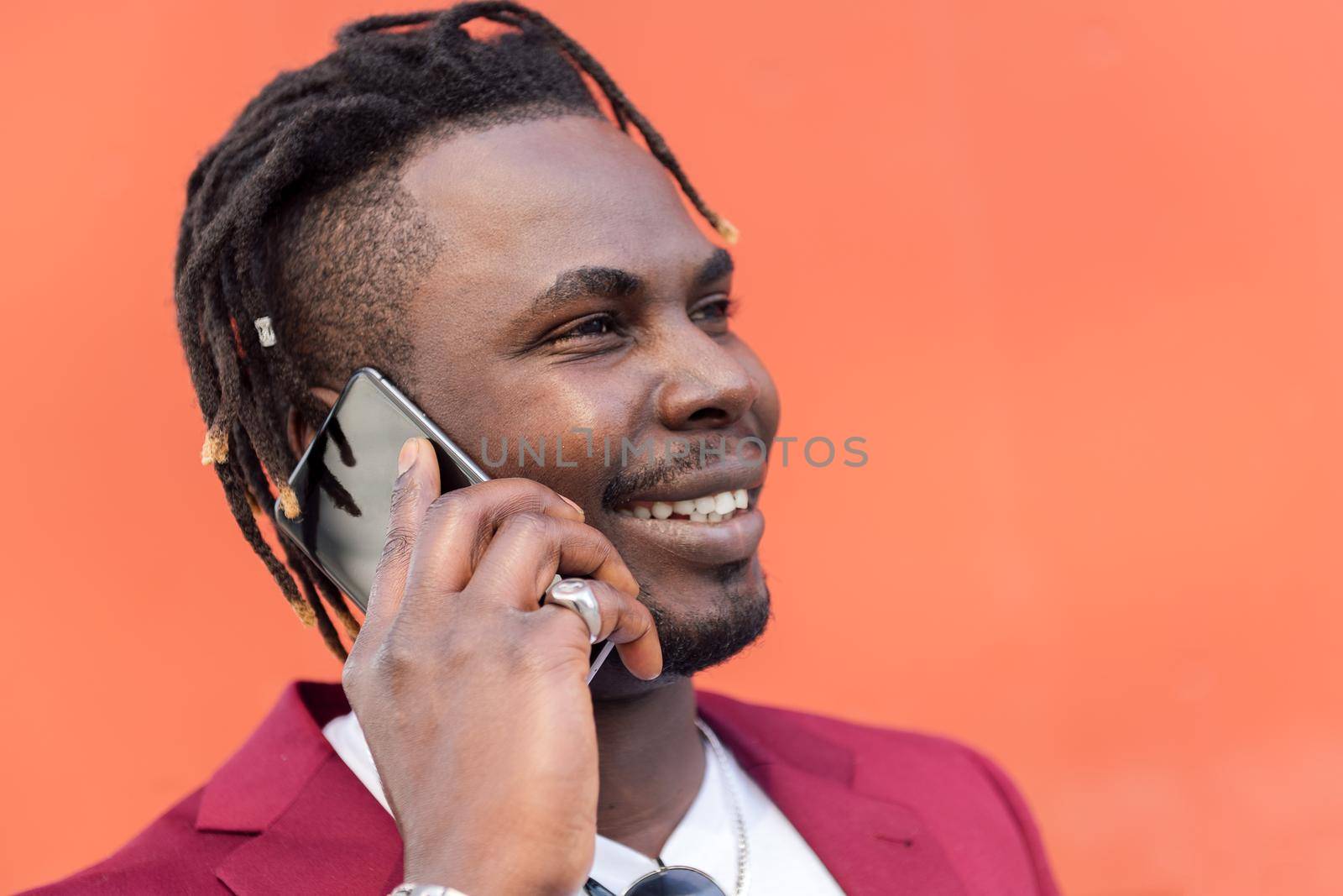 portrait of a stylish black businessman in suit smiling and talking on phone in front of red background, copy space for text, concept of technology and communication