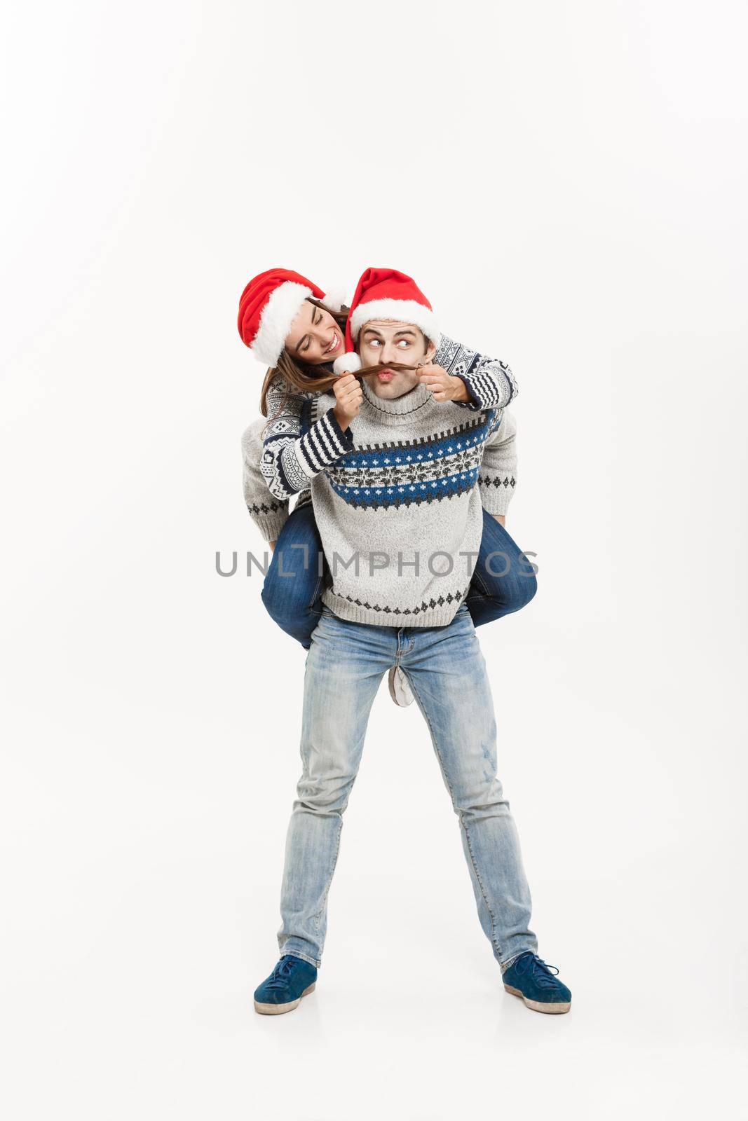Christmas Concept - Full-length Young happy couple in sweaters enjoying piggyback ride isolated on white grey background.