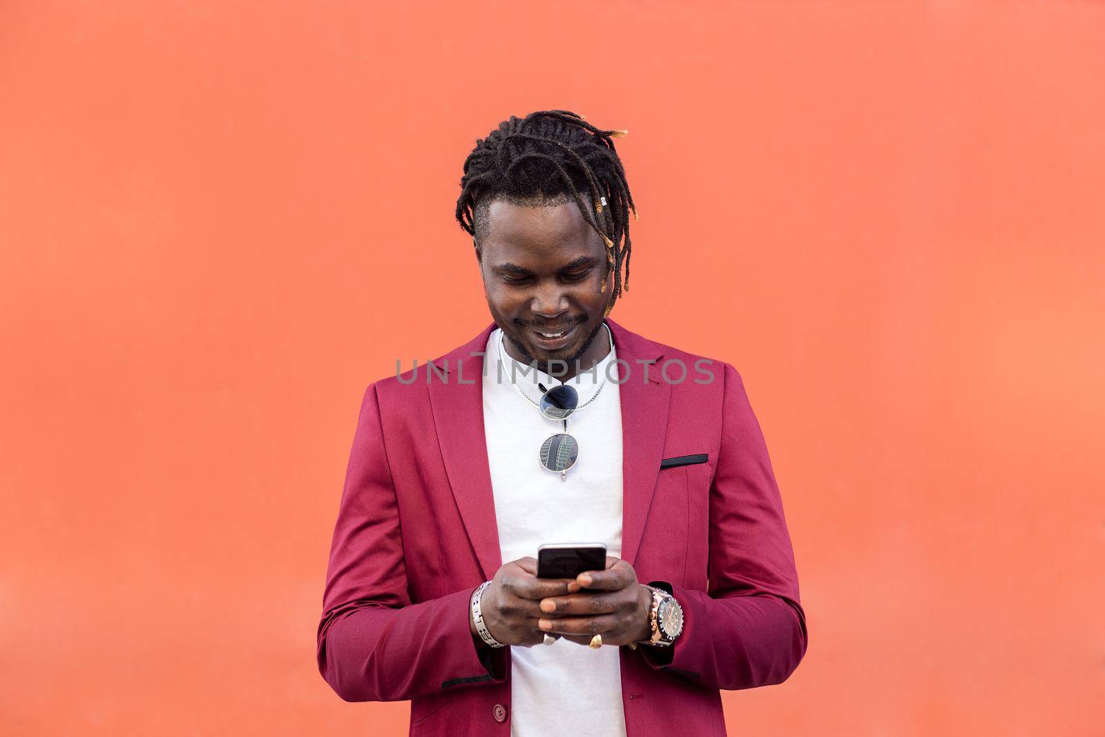 stylish black businessman in suit typing a message on his smart phone in front of a red background, copy space for text, concept of technology and communication