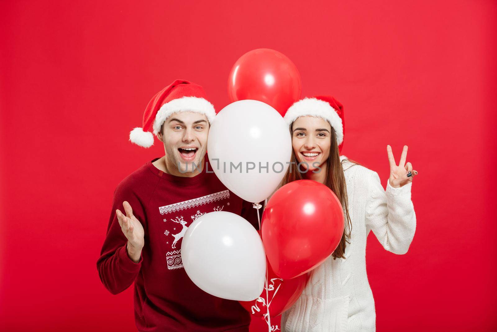 Christmas concept - Portrait of a romantic young couple with christmas balloon over red studio background.