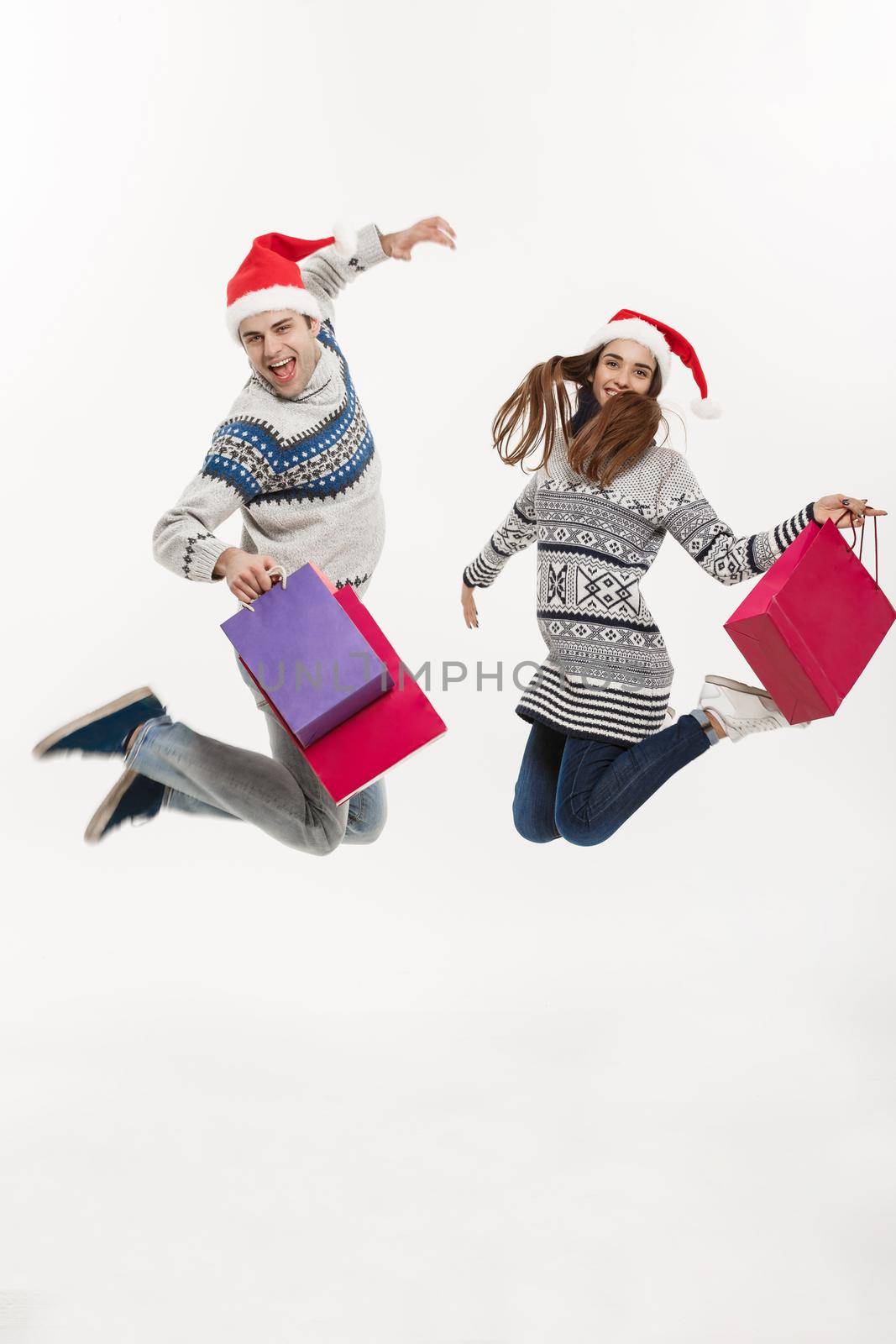 Christmas Concept - Full length Young attractive couple holding shopping bags and jumping isolated on white grey background. by Benzoix