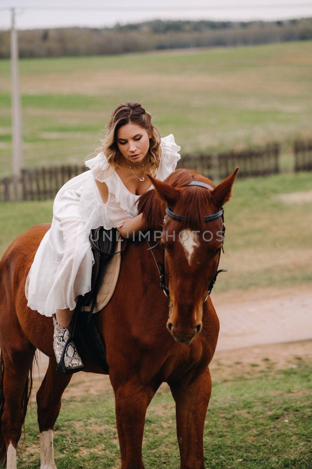 A woman in a white sundress riding a horse in a field.