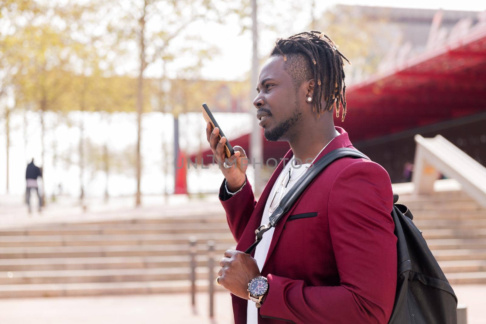 stylish black businessman records a voice message on his smart phone walking through the city, copy space for text, concept of technology and communication