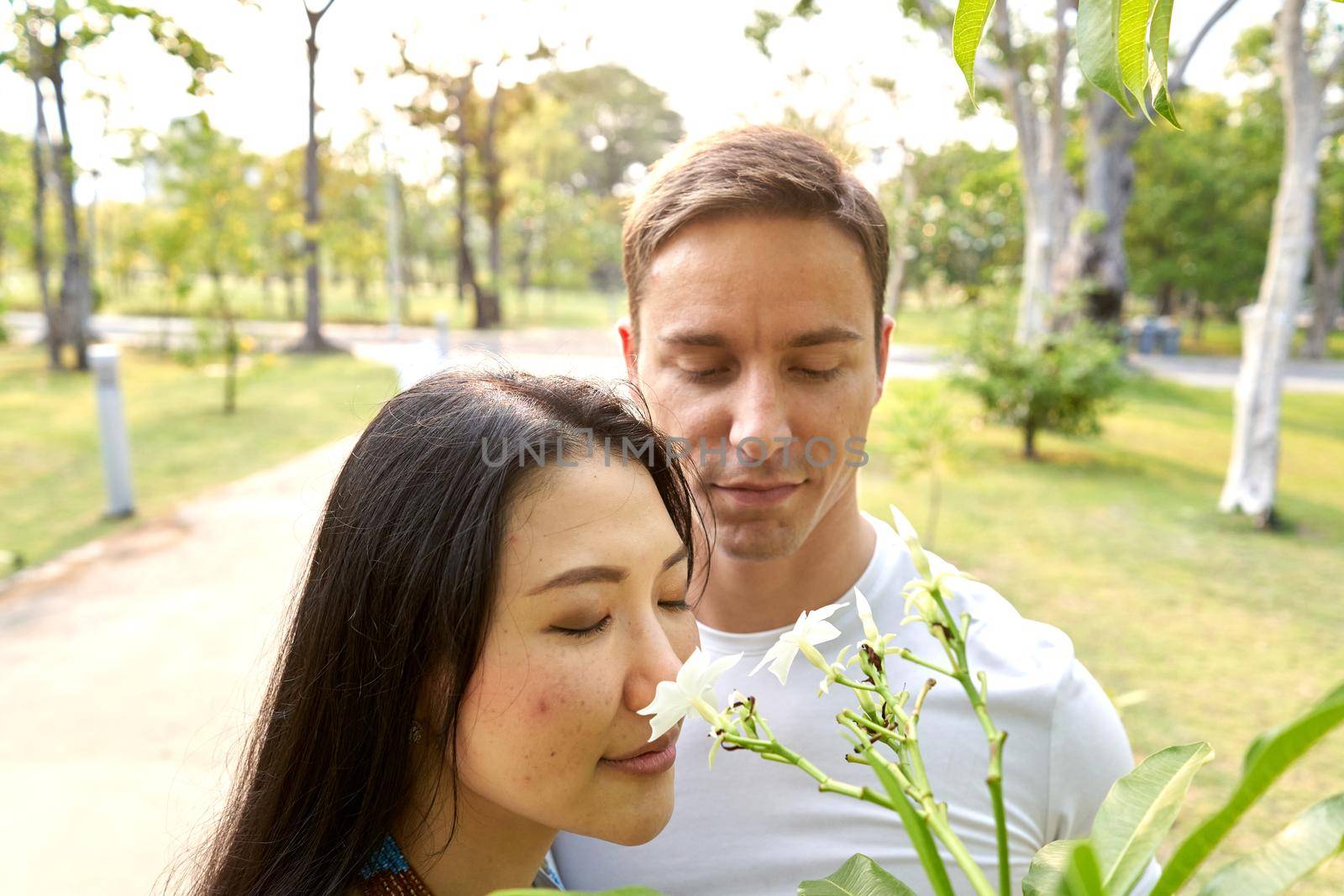 Multicultural couple smelling tropical flowers in an urban park by WesternExoticStockers