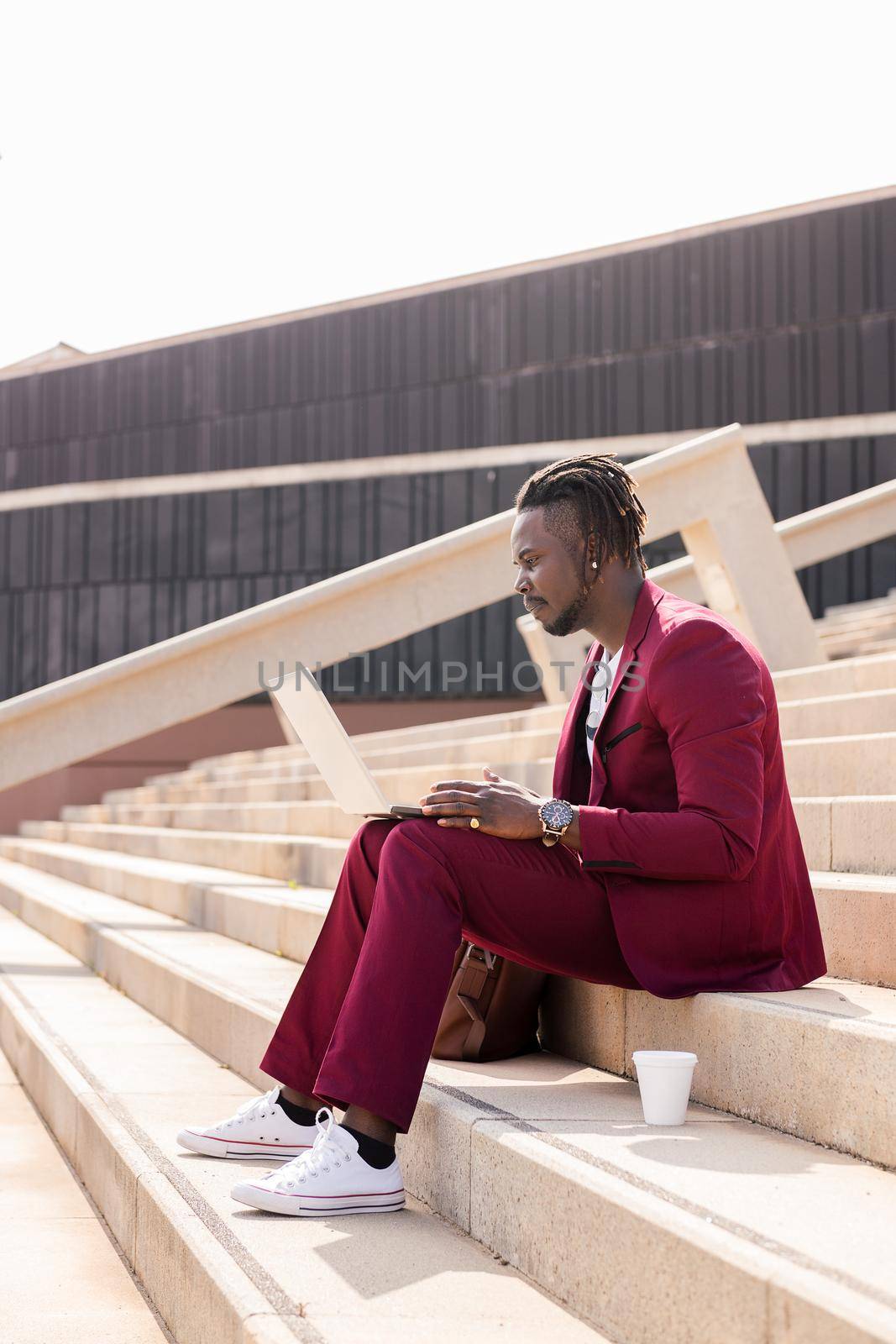 elegant african businessman works with his laptop sitting on a staircase in the city, technology and remote work concept, copy space for text