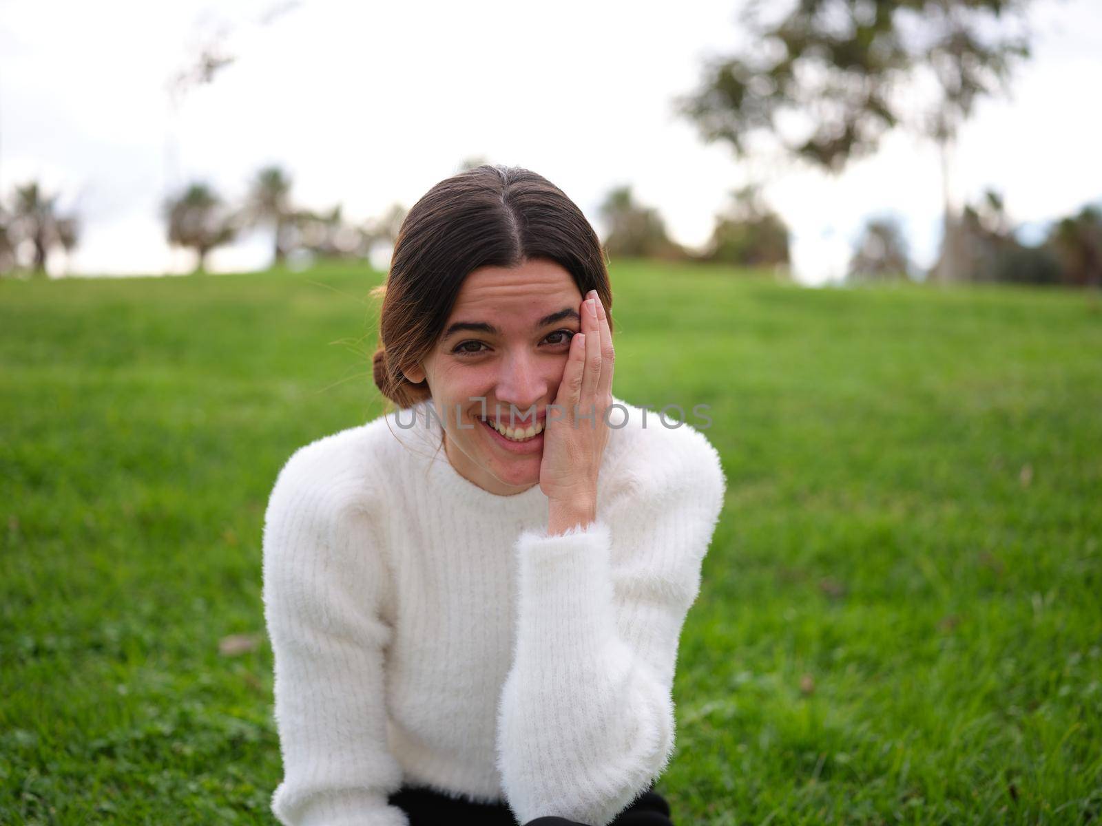 Front view of a happy young woman in the park looking at the camera touching her face with her hand while laughing.. Concept of emotions.